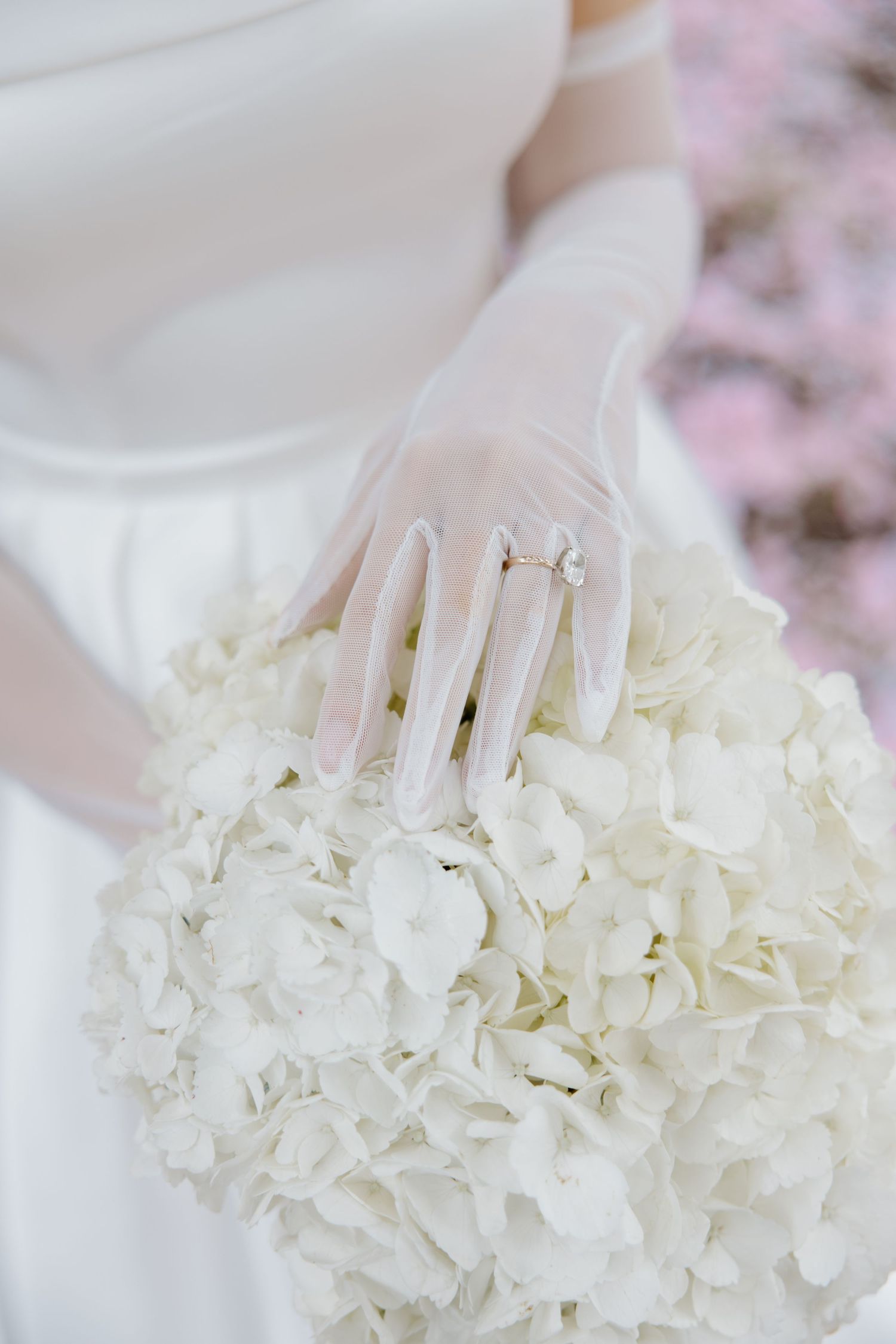 Close up of a white hydrangea bridal bouquet with elegant sheer gloved hand showing wedding ring.