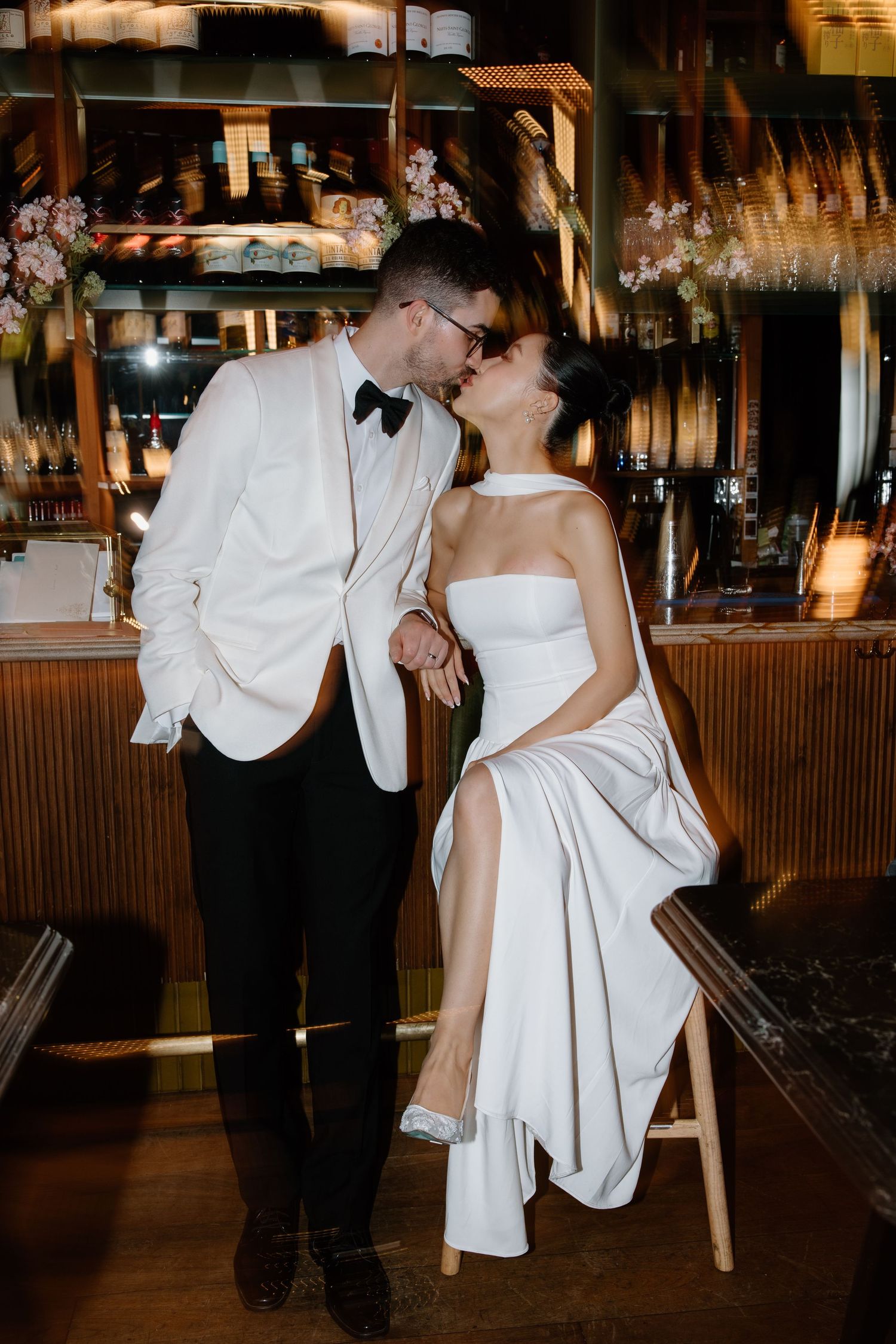 Couple shares romantic kiss at bar reception, with bride in elegant white dress and groom in white dinner jacket.