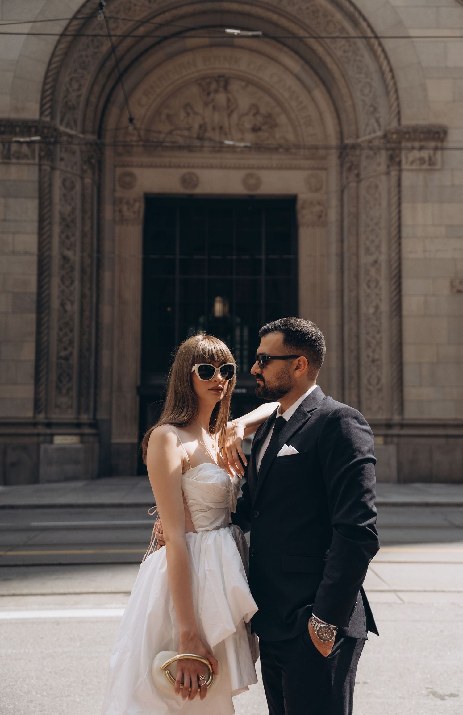 A romantic moment captured between a couple standing in front of grand stone archways at a historic building.