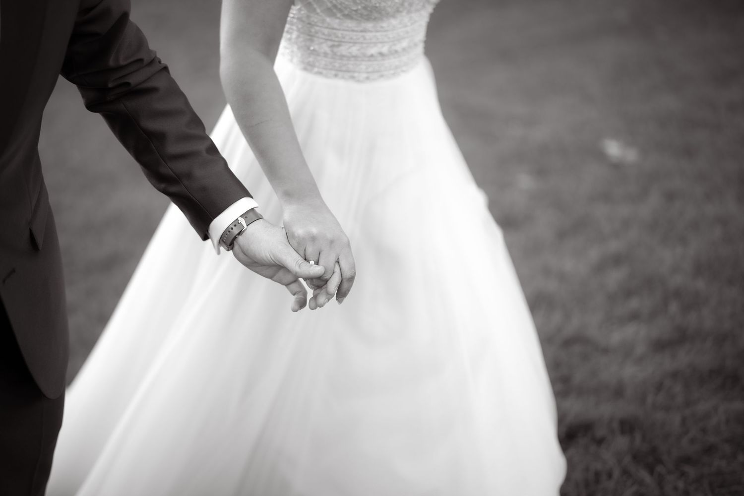 Black and white image showing hands holding while wearing formal wedding attire.