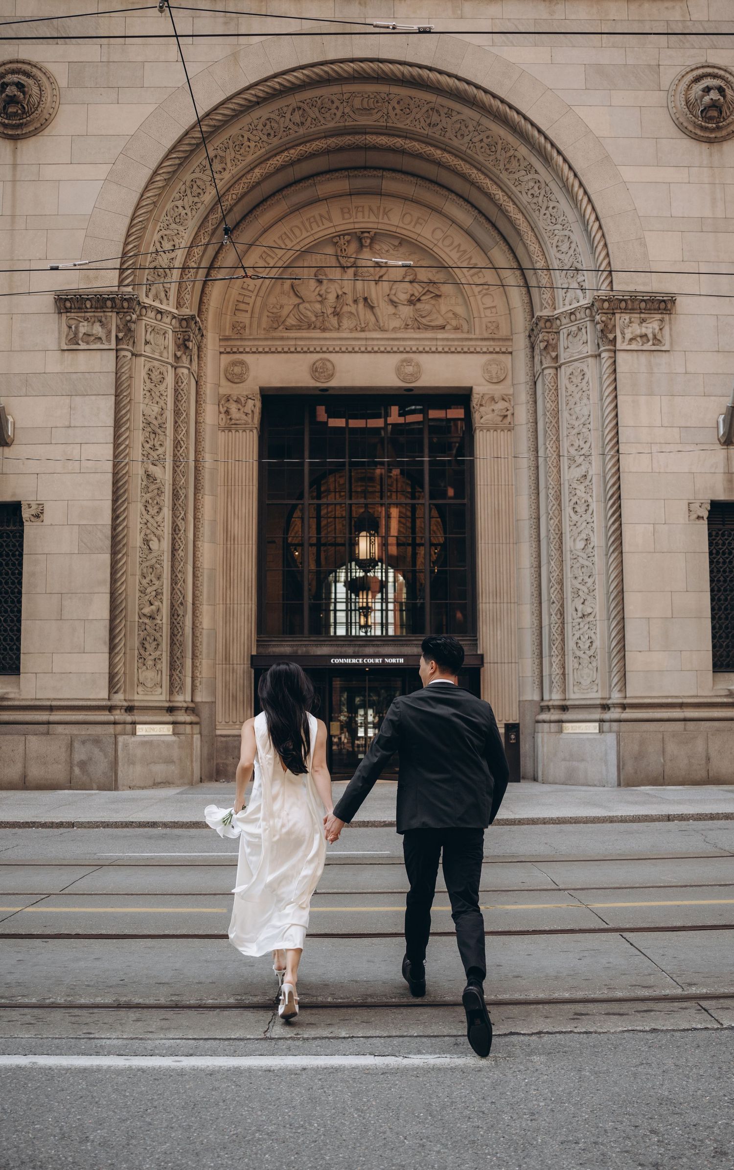 A couple walks hand in hand towards an ornate arched entrance of a historic stone building.