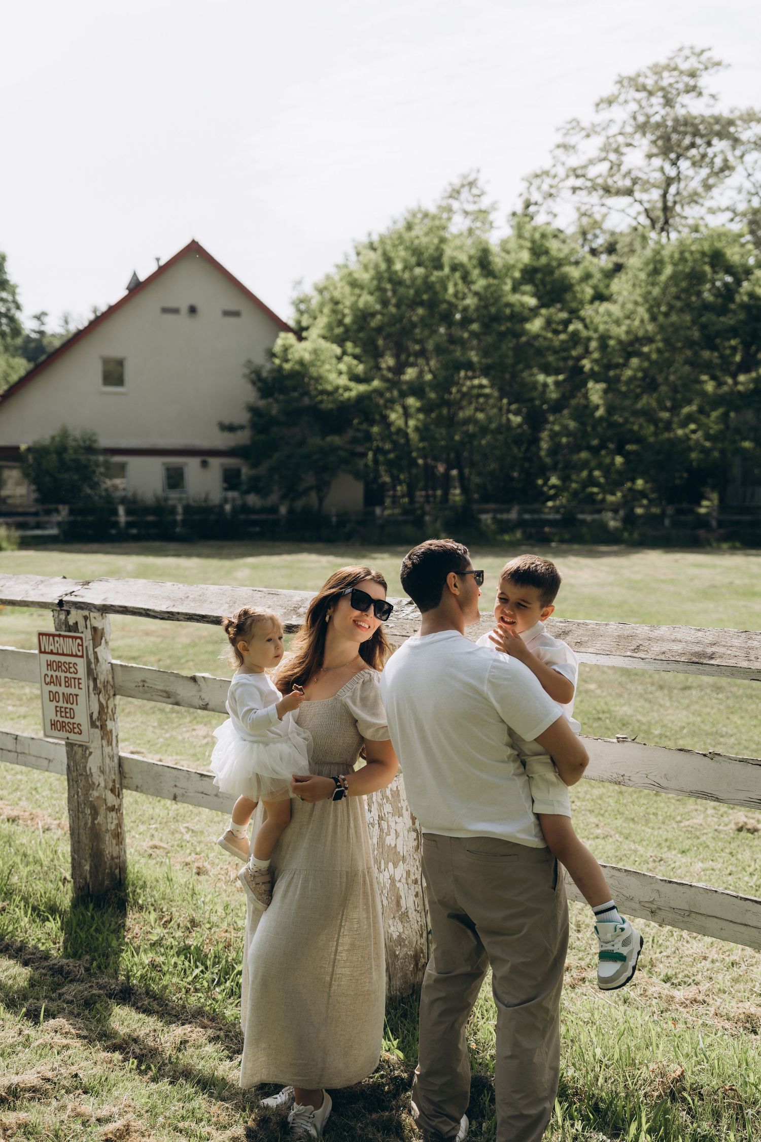 Four images show a couple in neutral-toned outfits walking along a rustic wooden fence in a sunlit outdoor setting.
