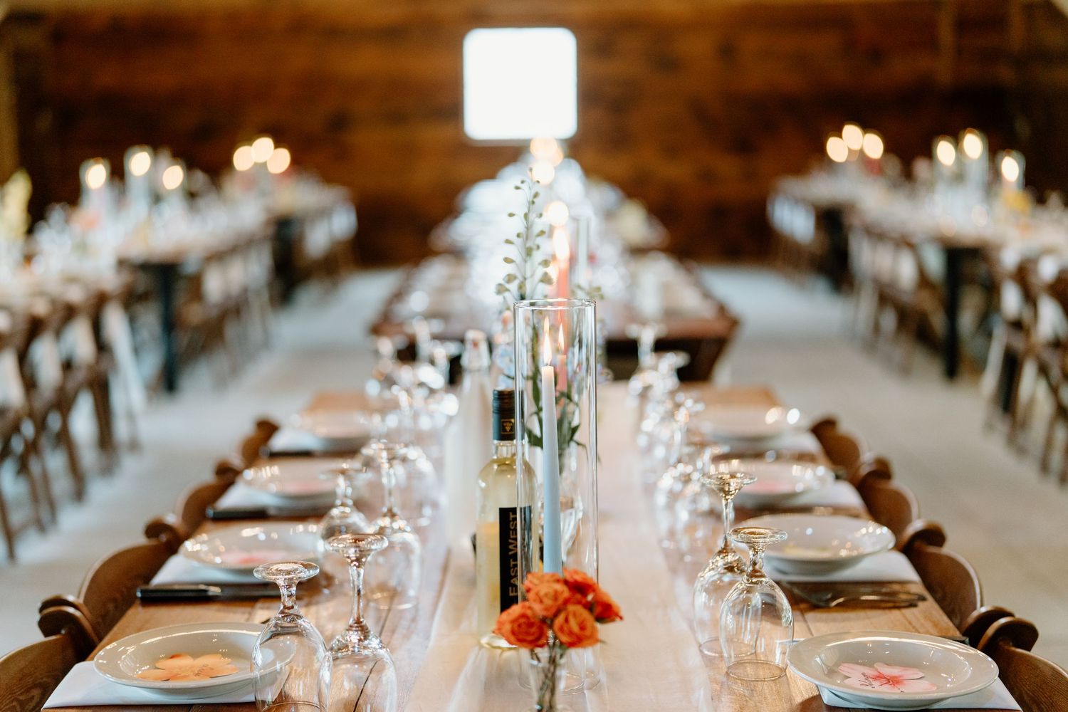 Long banquet tables set with elegant place settings and floral centerpieces in a rustic indoor venue.