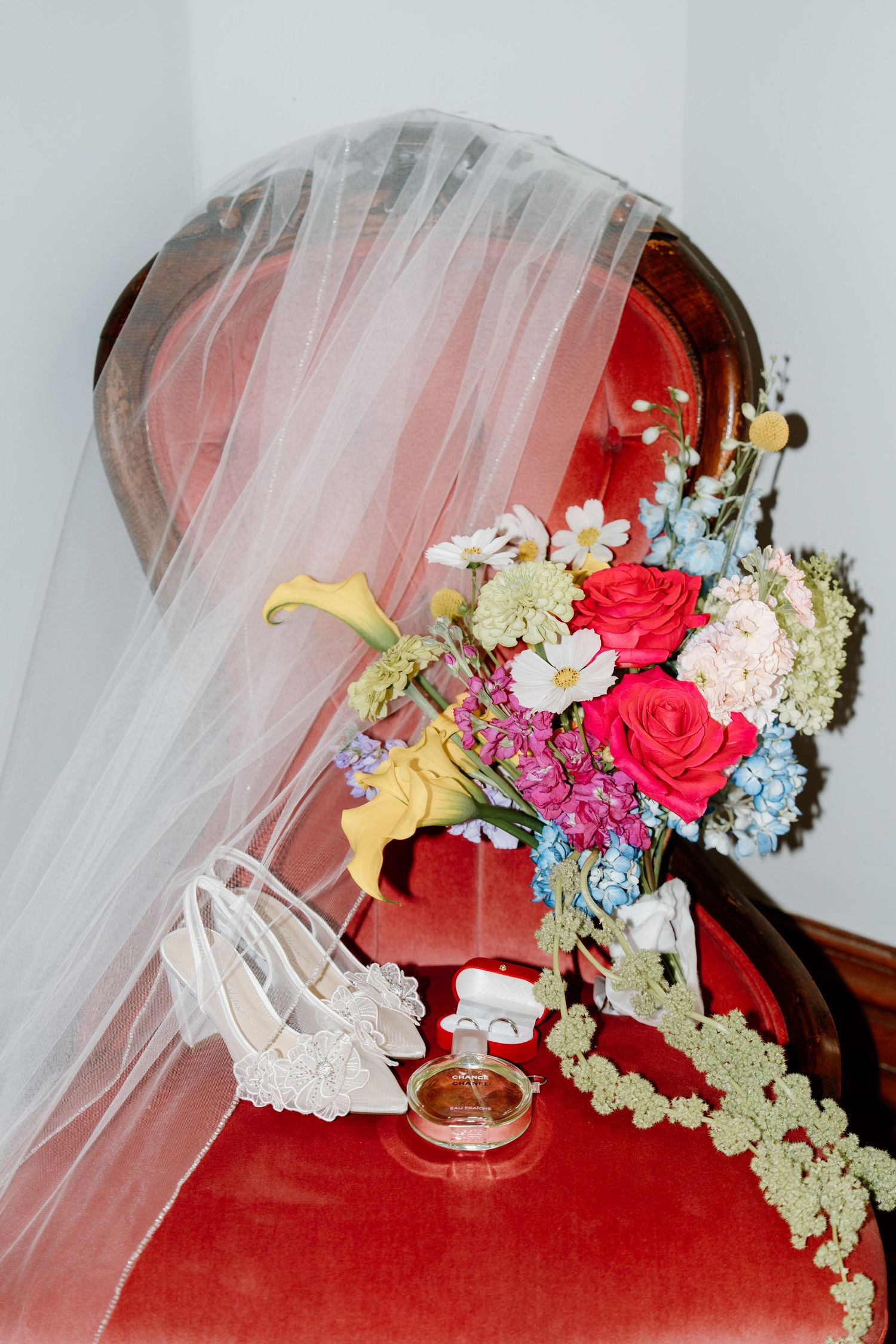 A floral arrangement with red roses, blue hydrangeas, and white flowers cascades down a red surface with delicate tulle veil.