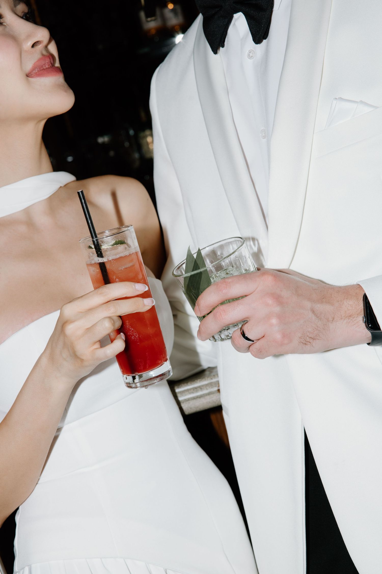 Two people in white formal attire toast with beverages at an elegant evening event.