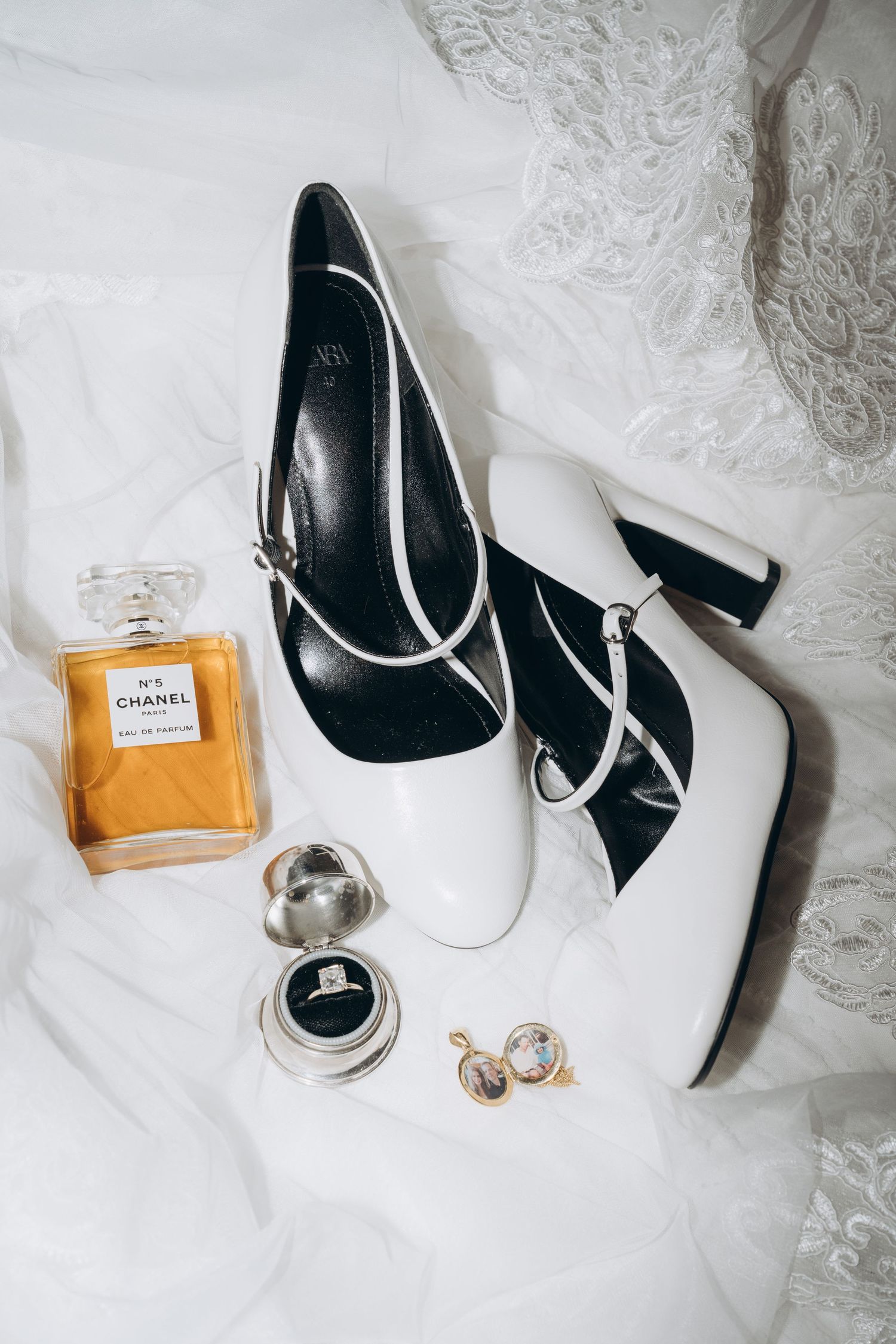 Elegant white bridal shoes and Chanel perfume bottle arranged on delicate lace fabric background for wedding details.