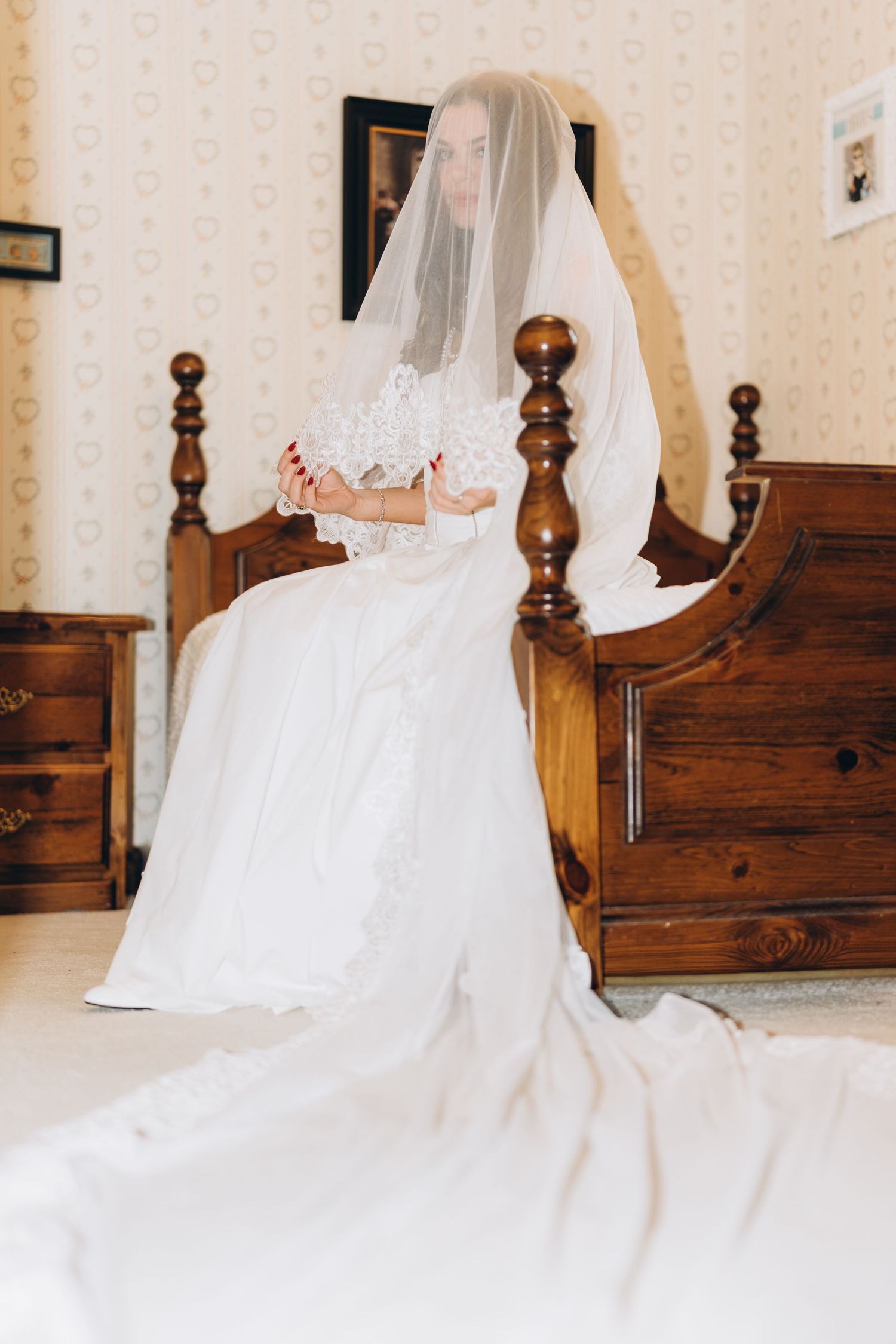 White wedding dress displayed on a wooden bed with delicate veil and flowing train.
