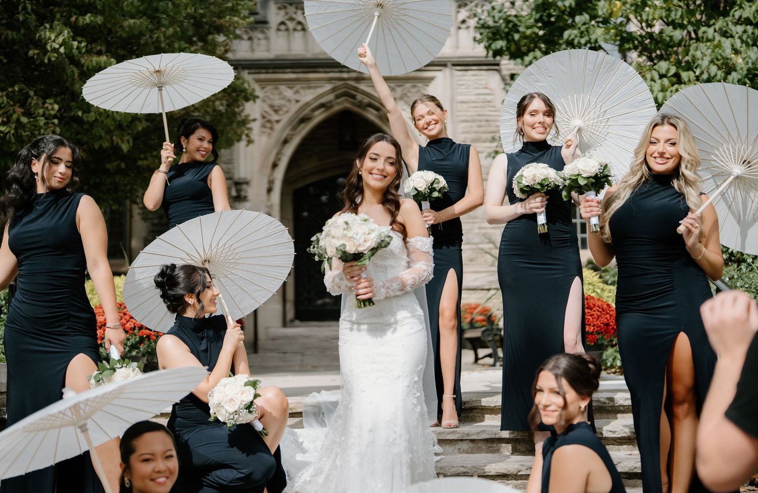 Wedding party poses with white parasols and navy blue dresses in an outdoor garden setting.