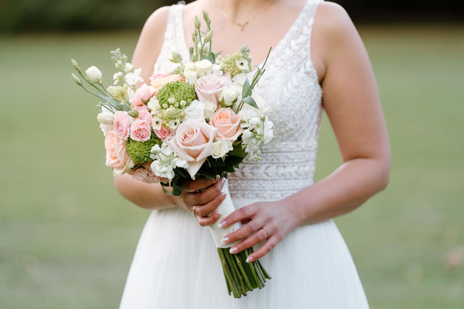 Close-up of bridal bouquet with blush roses and white flowers against lace bodice.