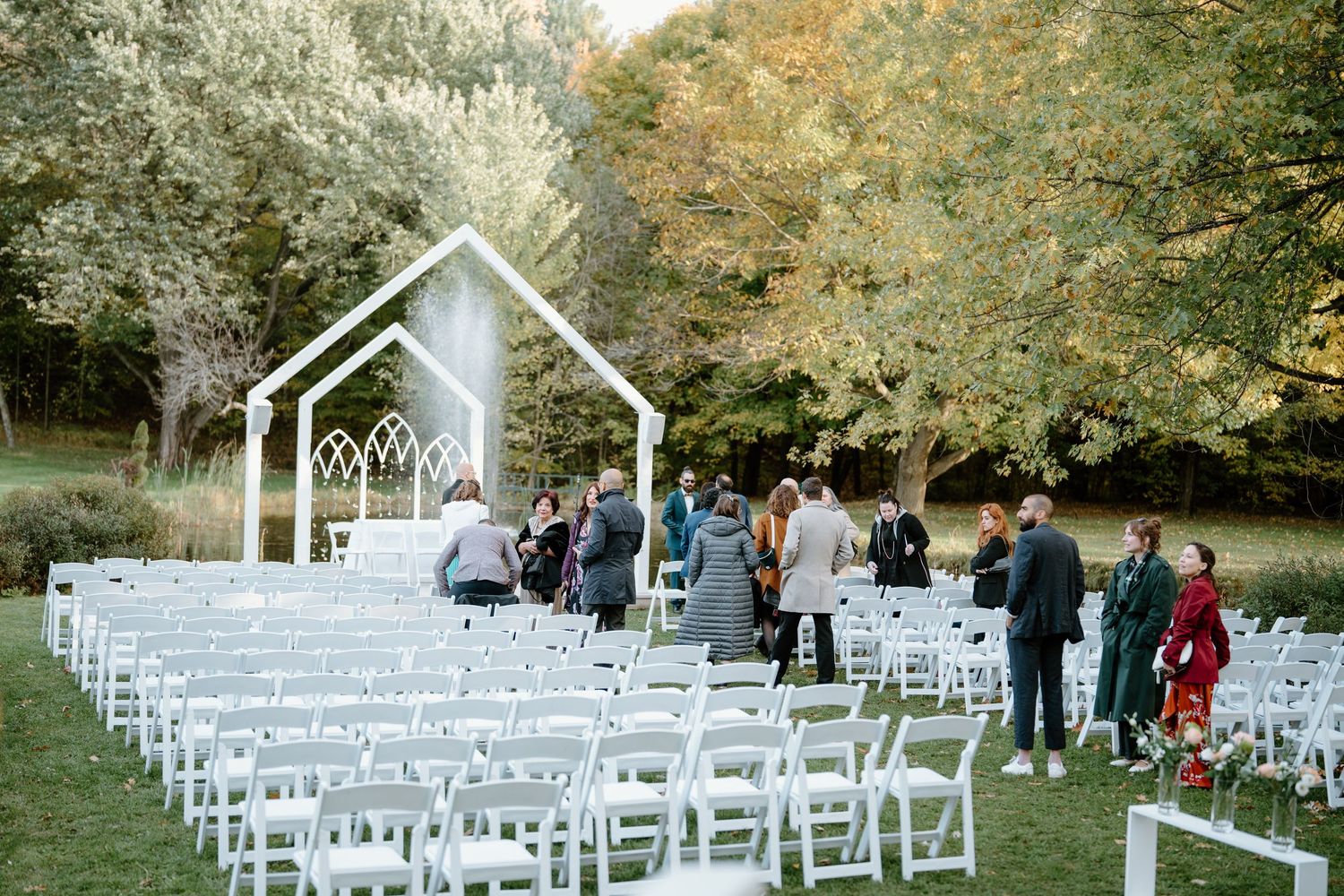 Outdoor wedding ceremony setup with white chairs and modern chapel structure surrounded by autumn trees.