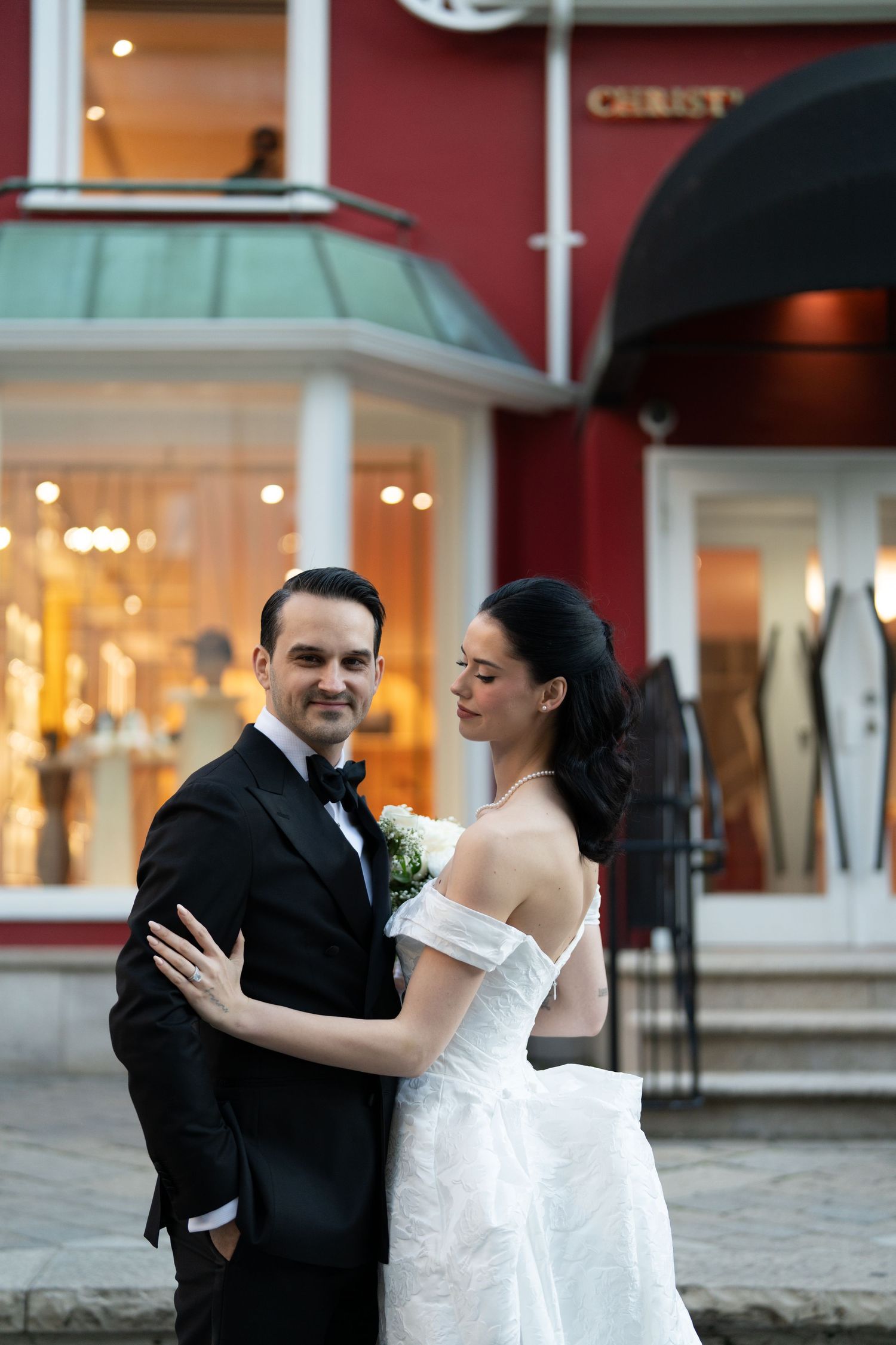 A couple dances together outside a storefront, with the bride in a white dress and groom in black suit.