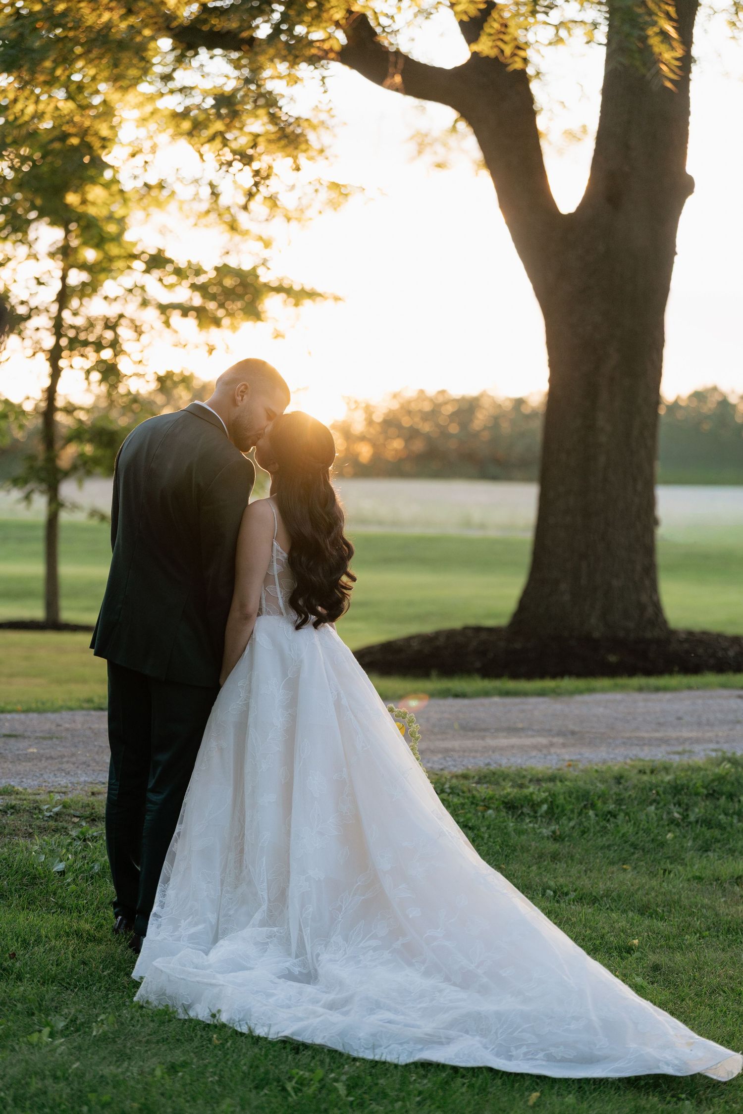 A romantic sunset wedding portrait shows a couple embracing under a large tree with golden light filtering through.