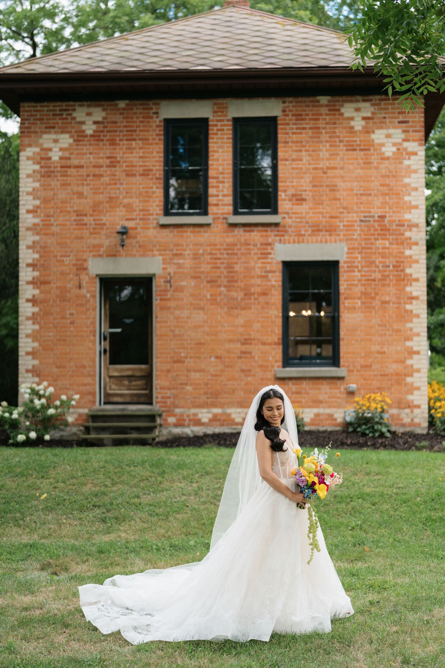A flowing white wedding dress with a long train displayed against a rustic brick building exterior.