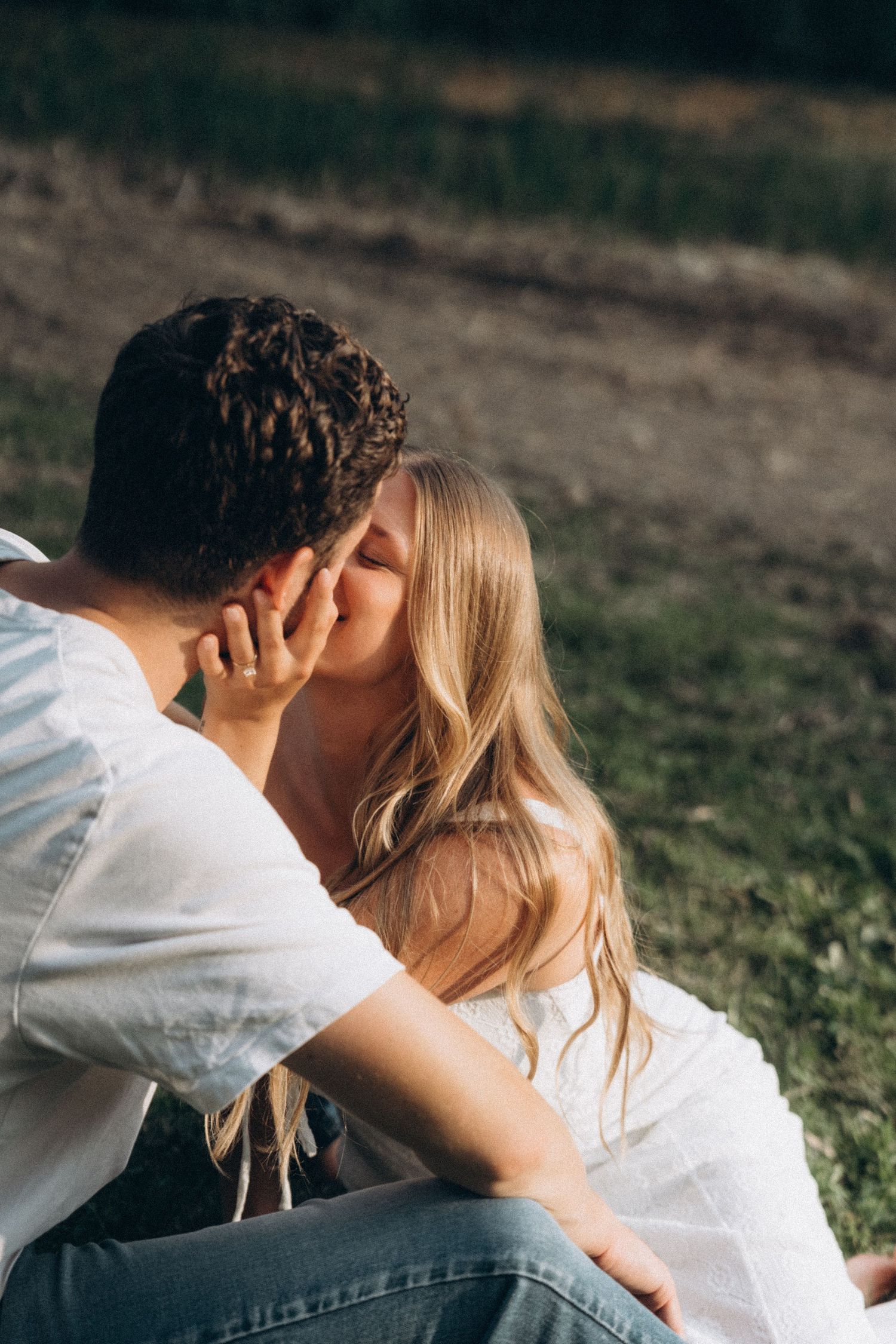 A romantic couple sharing an intimate kiss outdoors in a natural setting wearing white and dark clothing.