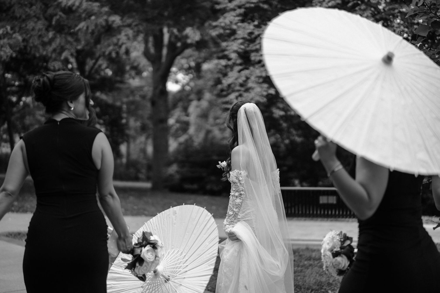 Wedding party poses with elegant white parasols in an outdoor garden setting.