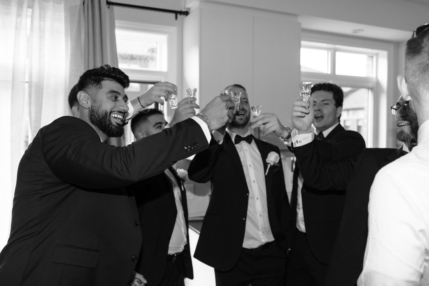 Black and white photo of groomsmen toasting with drinks at a wedding celebration.