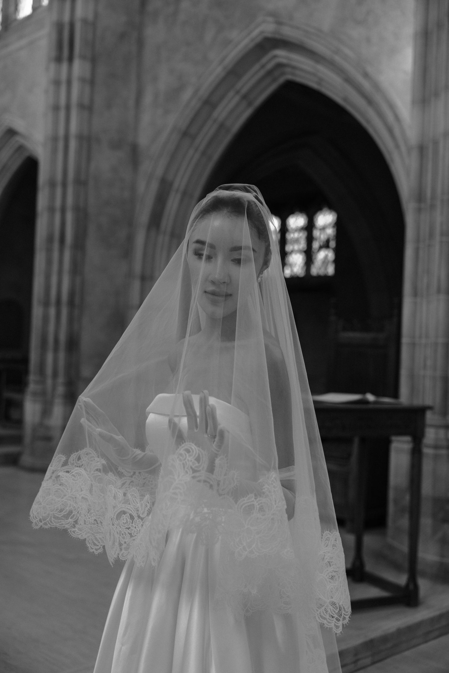 A bride in a classic white wedding dress and delicate lace veil stands in an elegant gothic church interior.