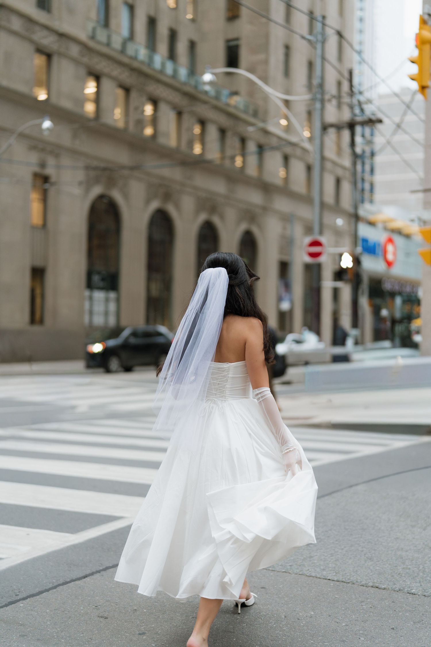 A bride in a white tea-length dress walks across an urban crosswalk in downtown Toronto, creating a series of artistic and can motion shots.