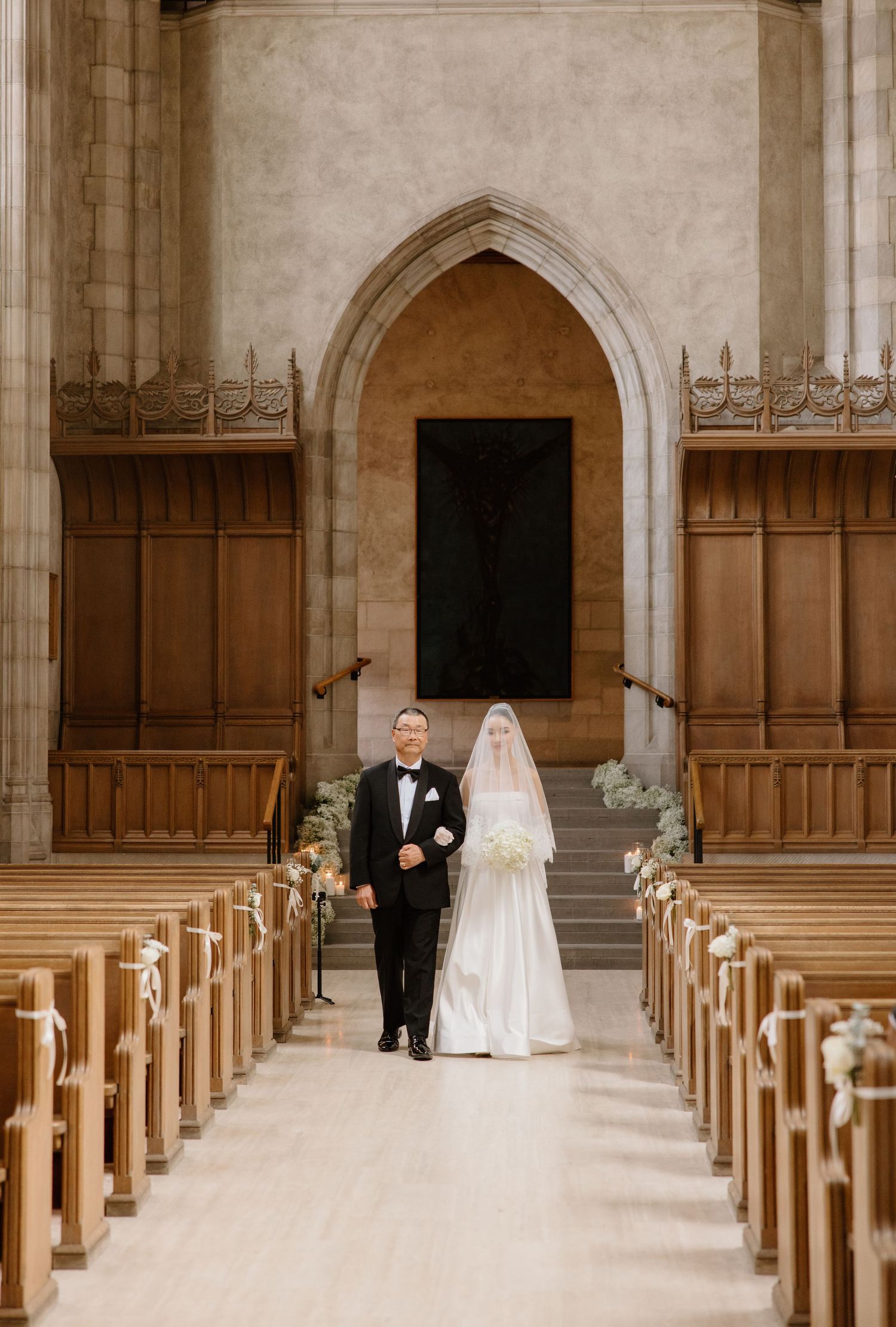 A long church aisle with wooden pews leads to an arched altar where figures stand for a traditional wedding ceremony.