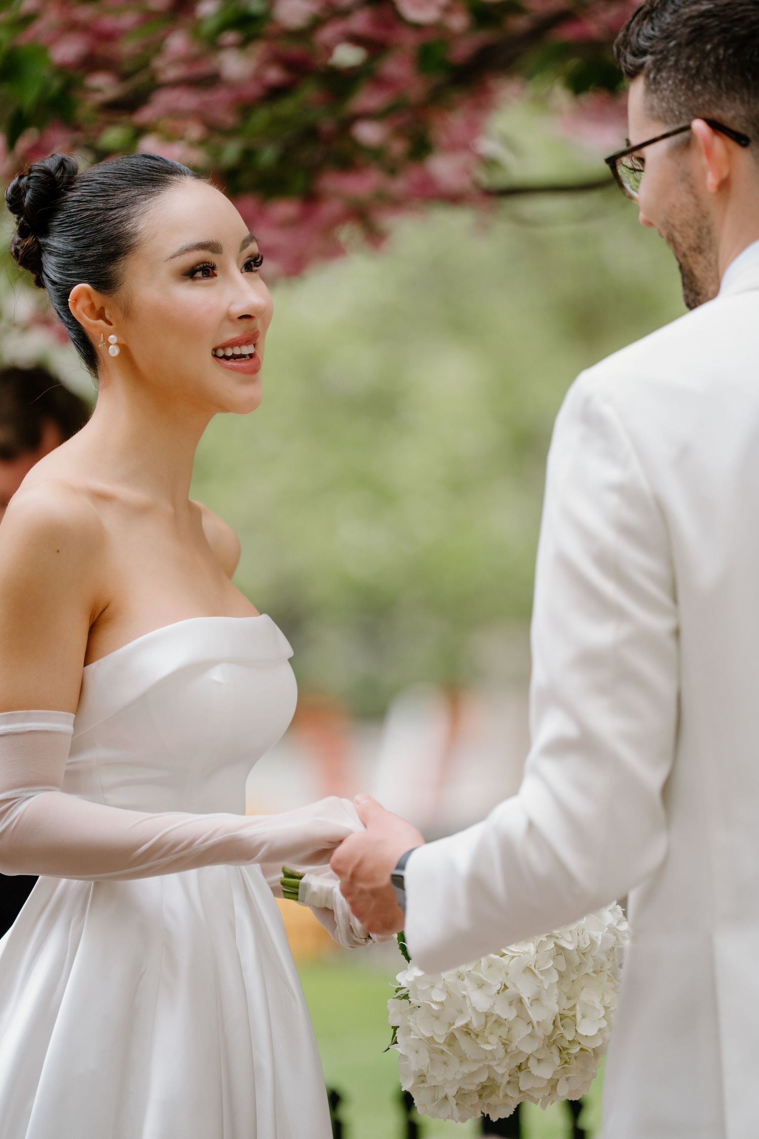 A joyful exchange between a couple during their wedding ceremony under blooming spring trees.