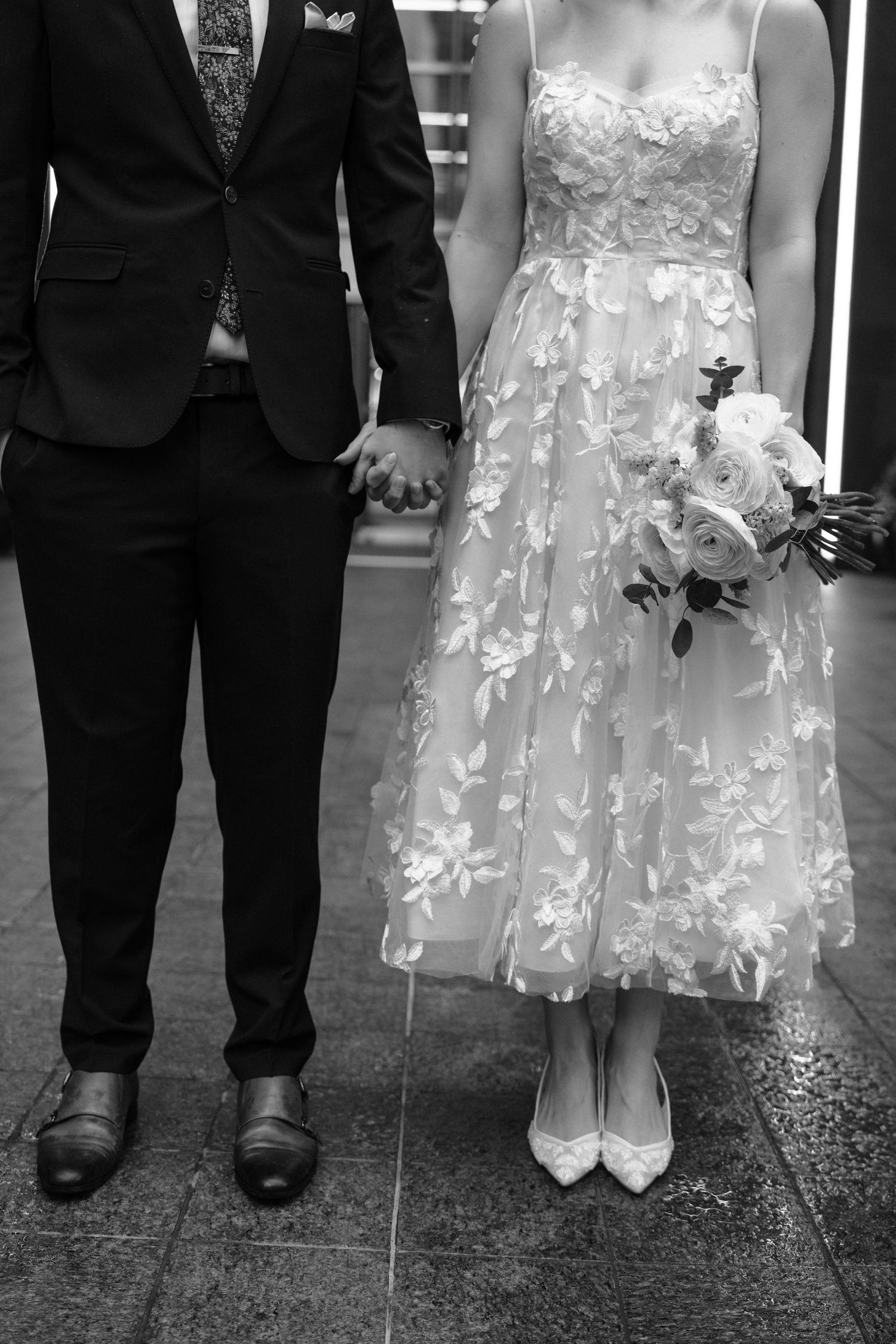 Black and white wedding photo showing feet and lower legs of couples wearing formal attire and dress shoes.