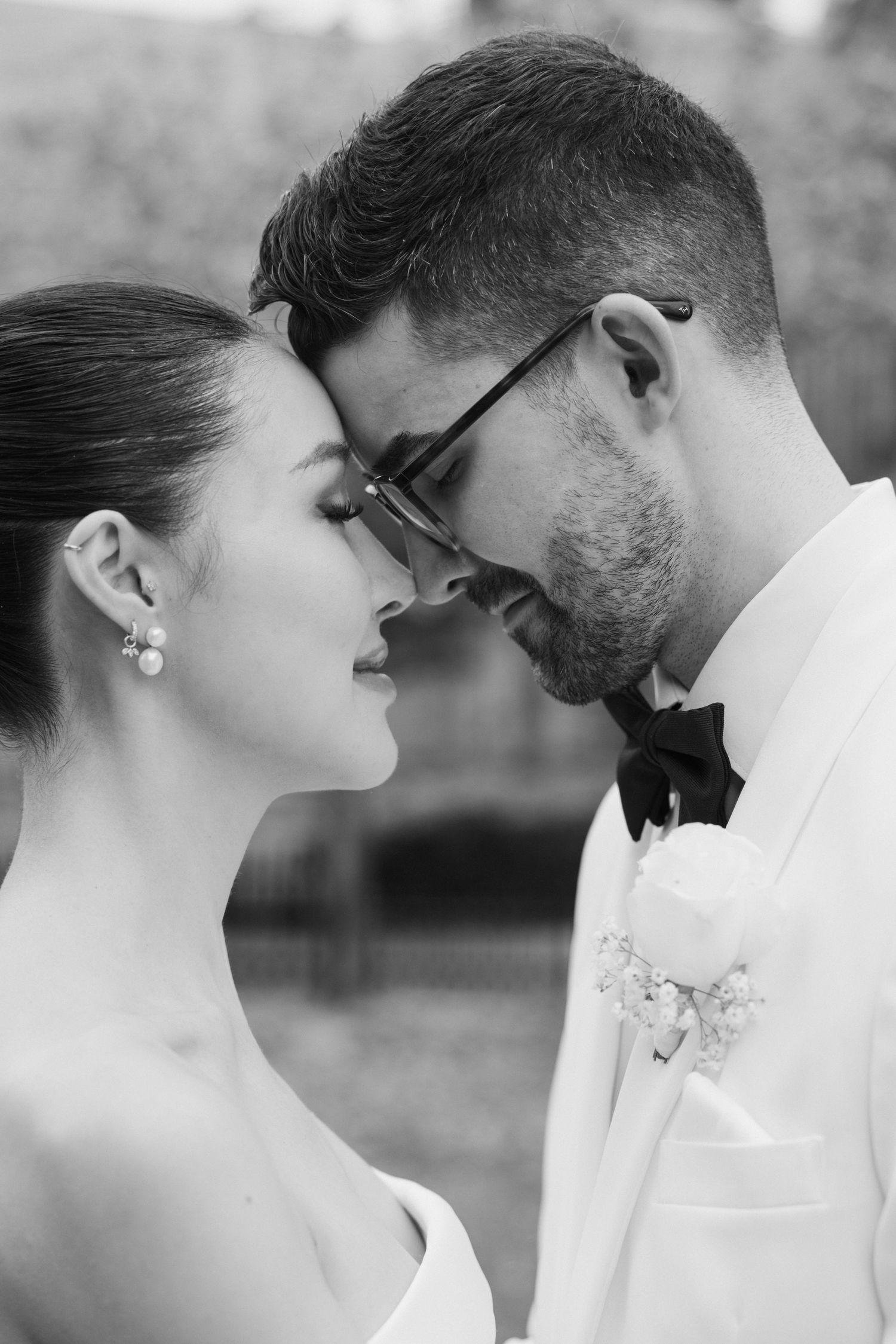 Black and white intimate wedding portrait of couple in formal attire sharing a tender forehead touch moment.