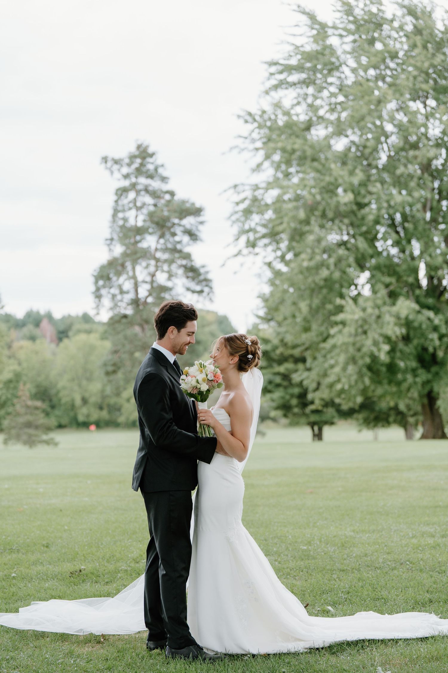 A romantic wedding scene unfolds on a serene grassy field with trees in the background.