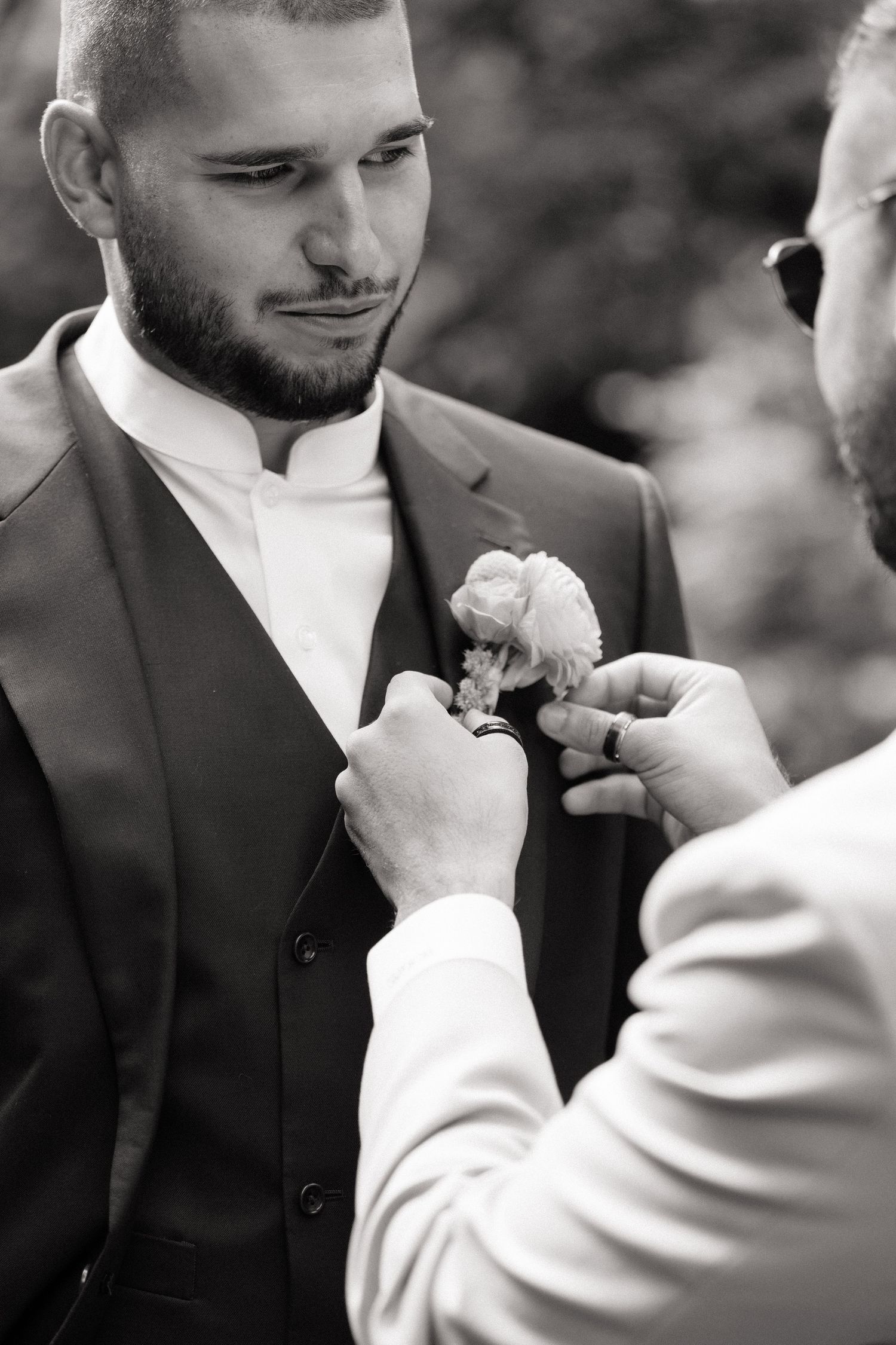 Black and white close-up sequence showing a boutonniere being pinned to a dark suit jacket.