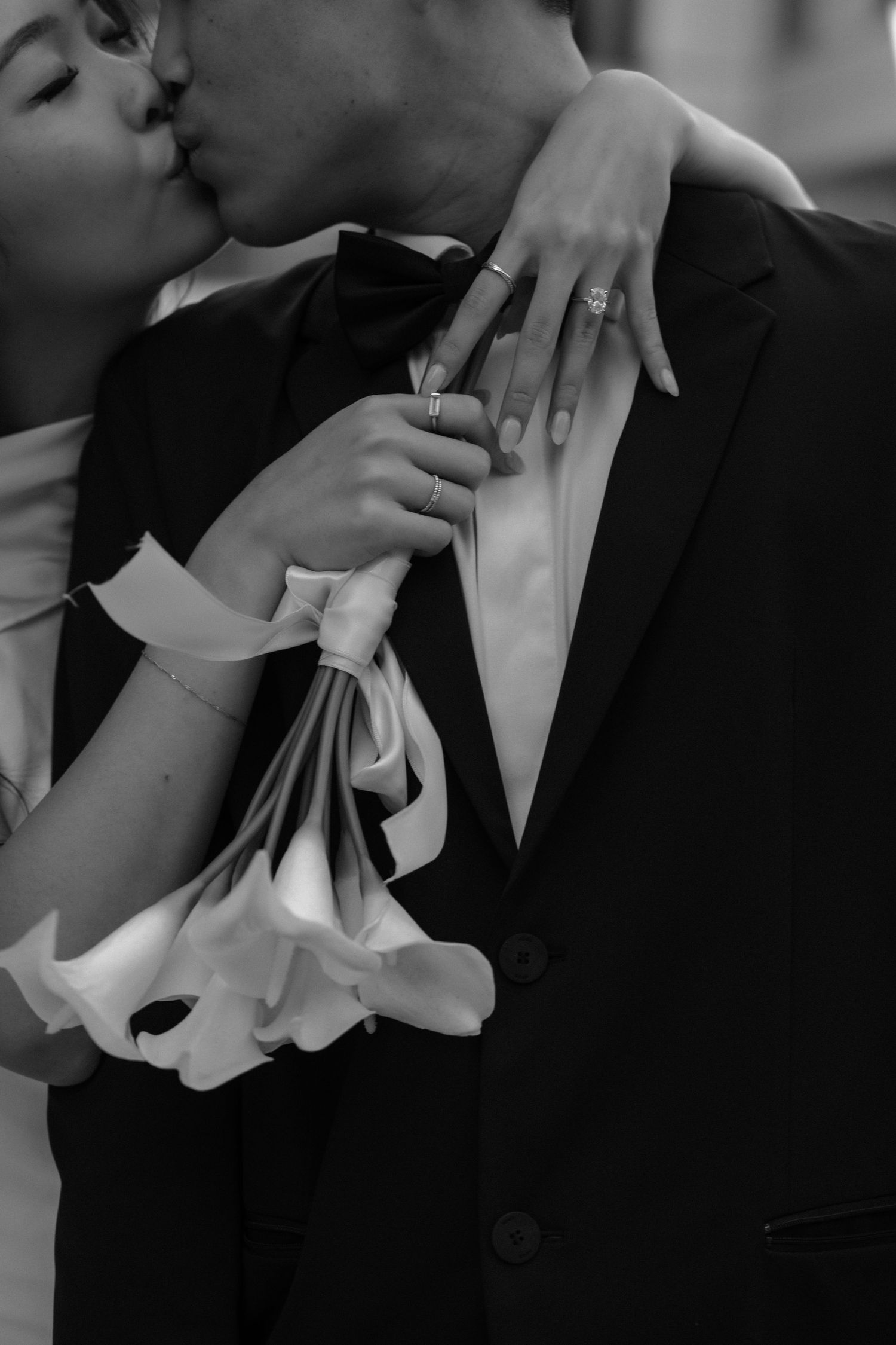 A romantic black and white photo showing hands holding calla lilies against a formal suit during an intimate moment.