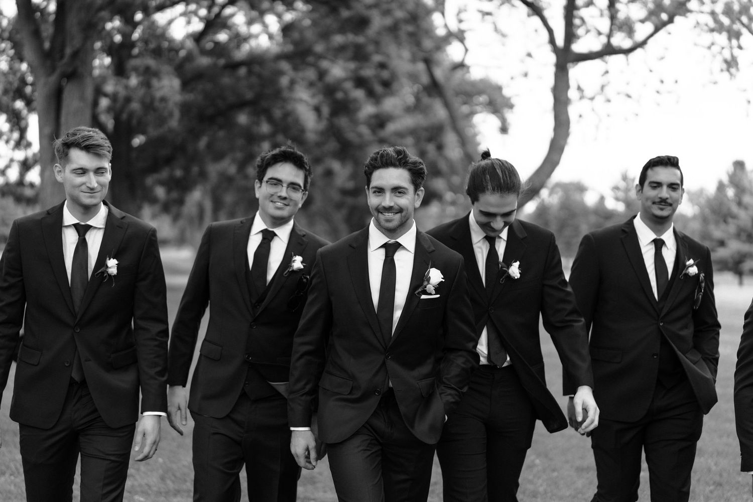 A black and white photo of groomsmen walking together outdoors in matching dark suits and ties.