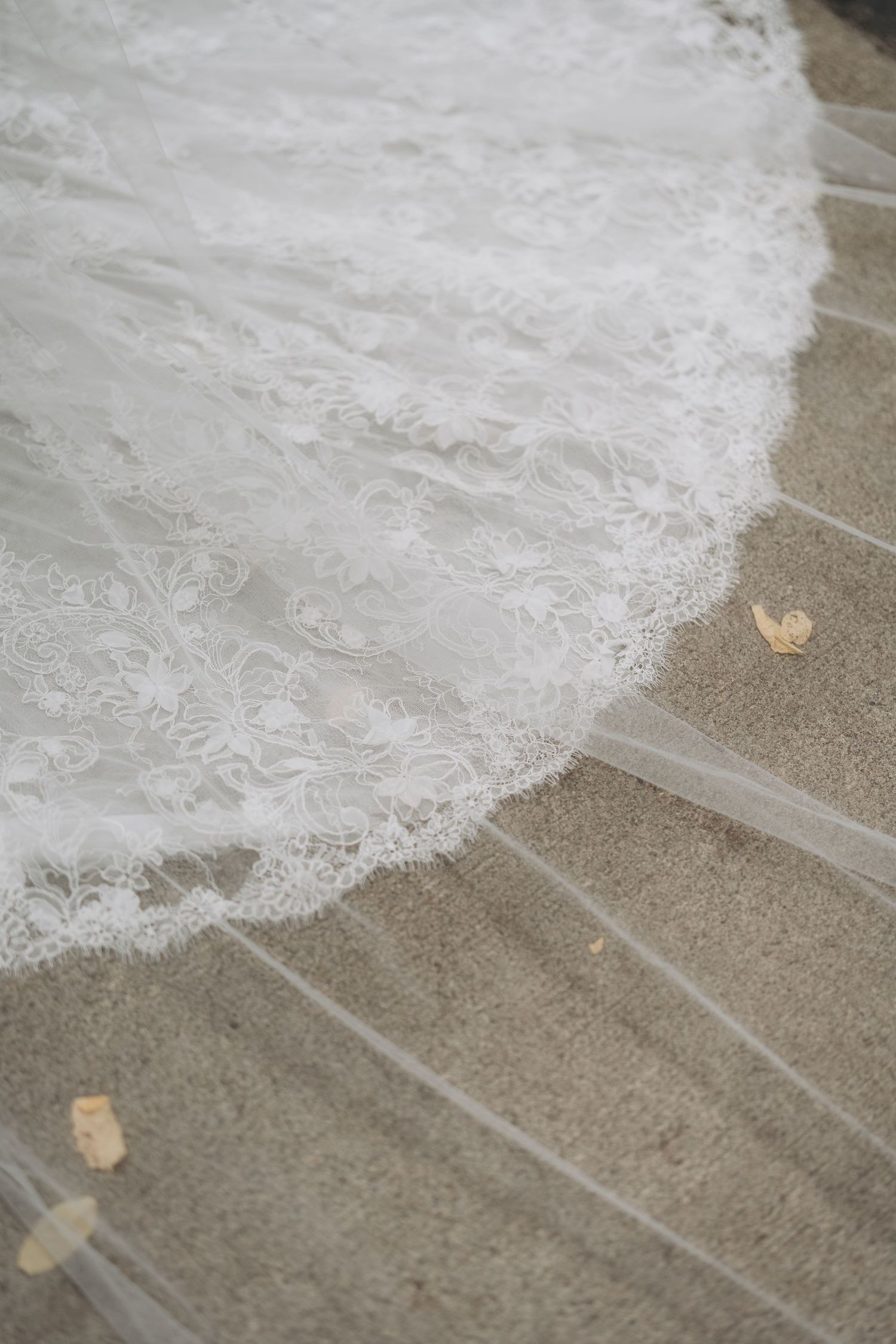 Delicate white lace wedding dress train flows across textured stone floor.