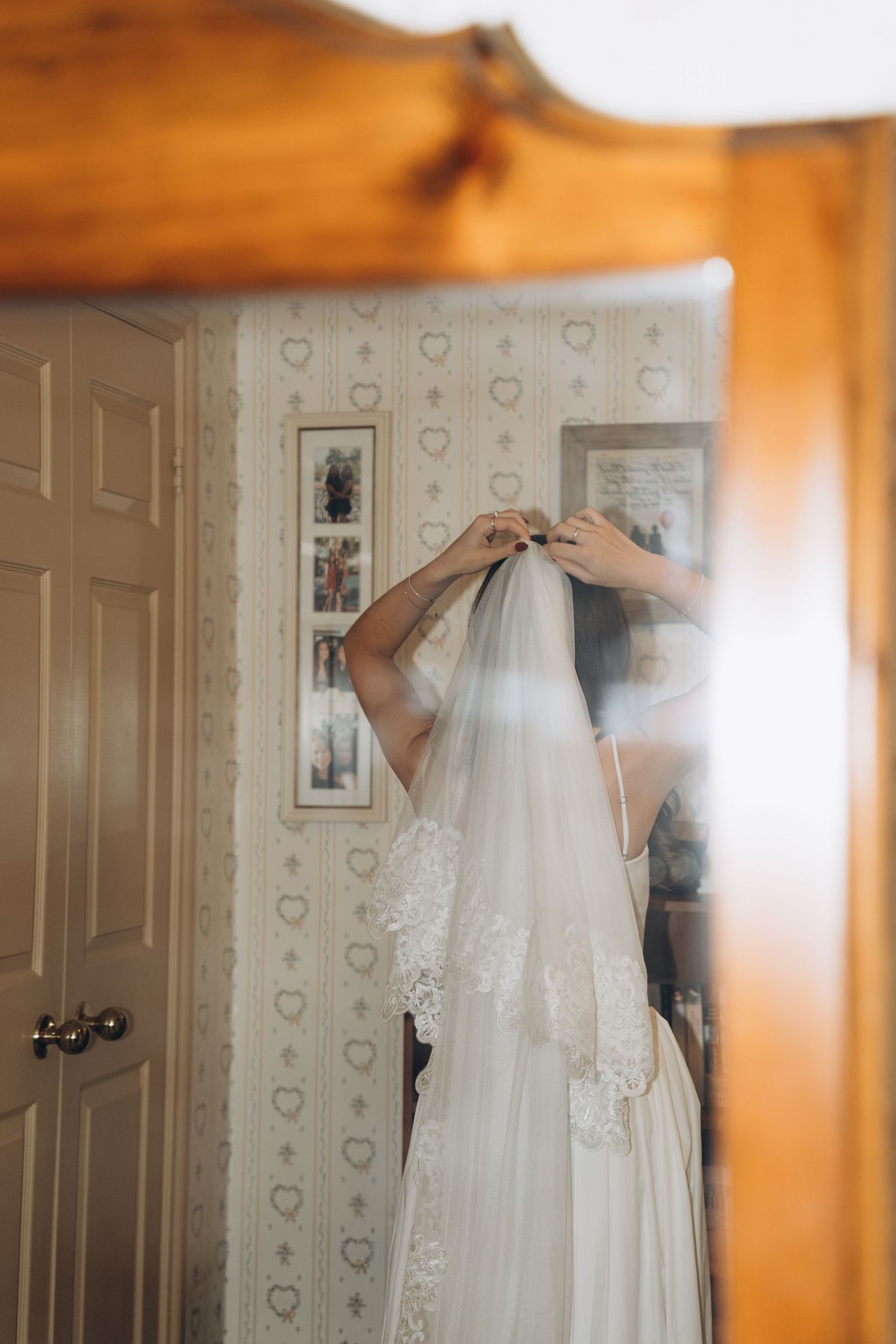 Wedding preparations show a bridal veil being delicately hung on display against a floral wallpaper background.