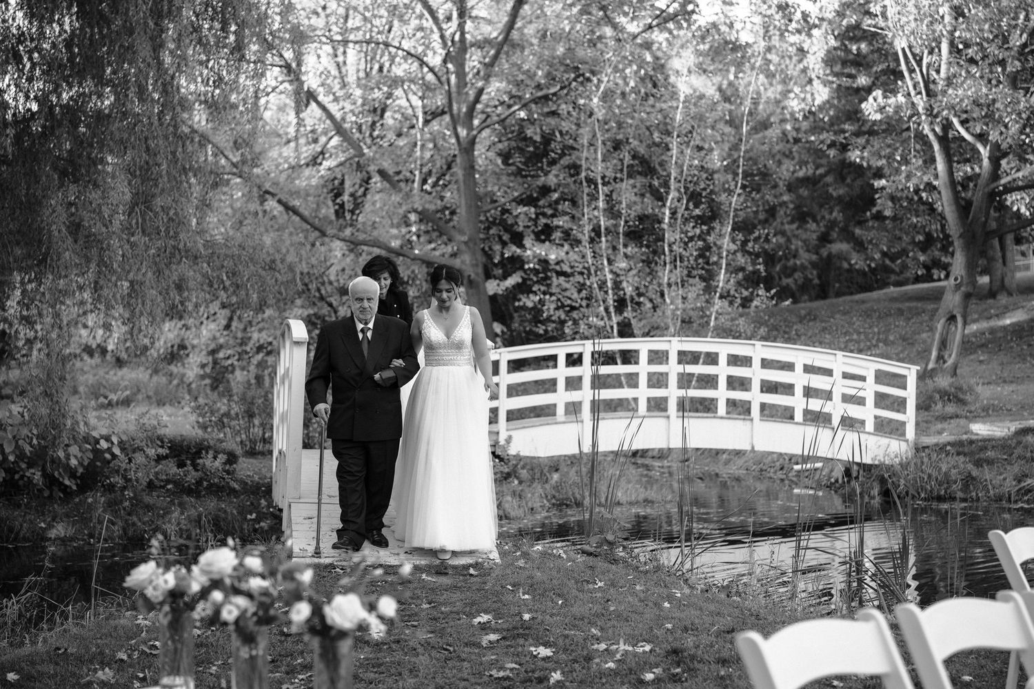 A black and white photo of a couple on a decorative white bridge in a garden setting.