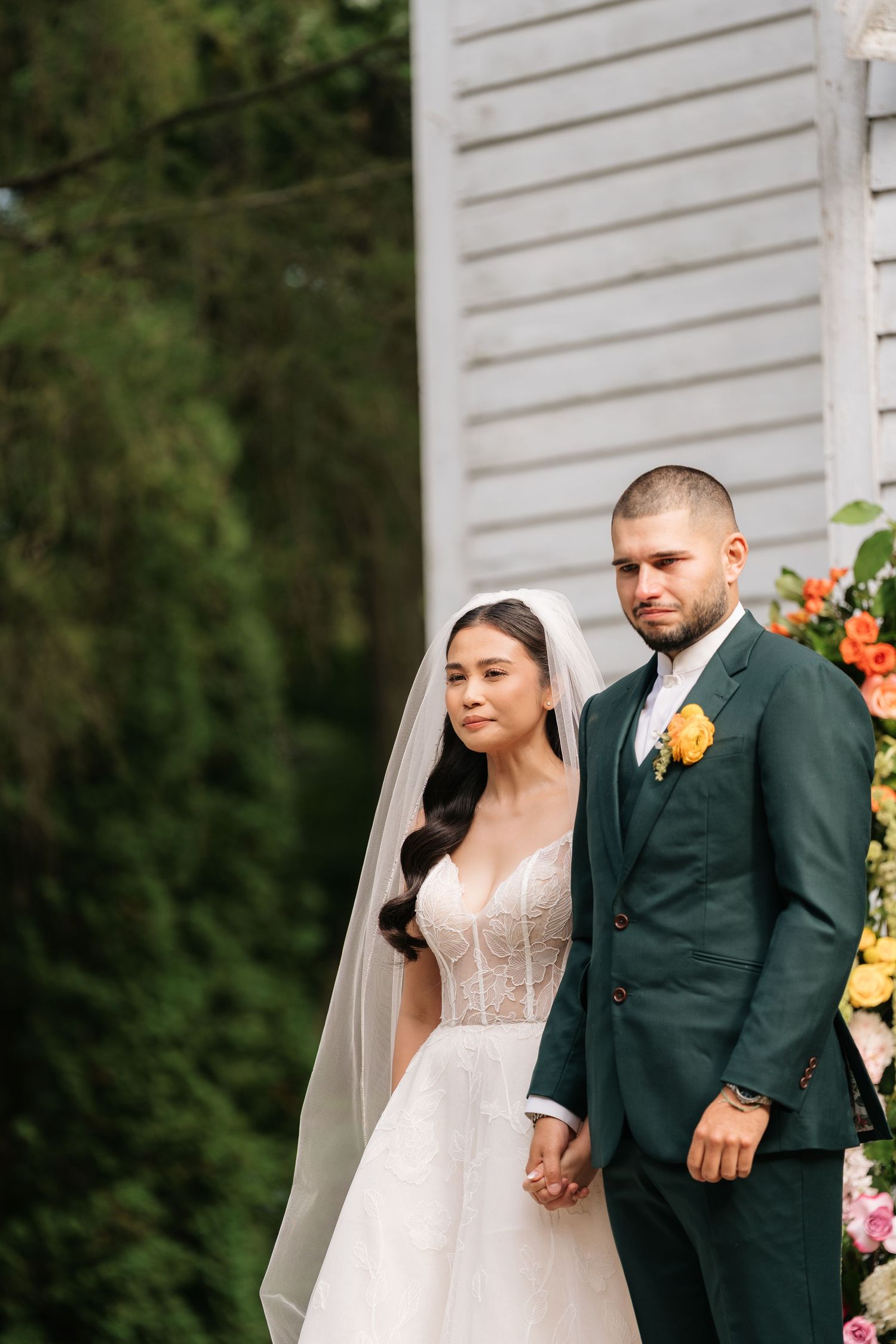 A wedding couple shares a romantic moment against a white wall with orange floral decorations.