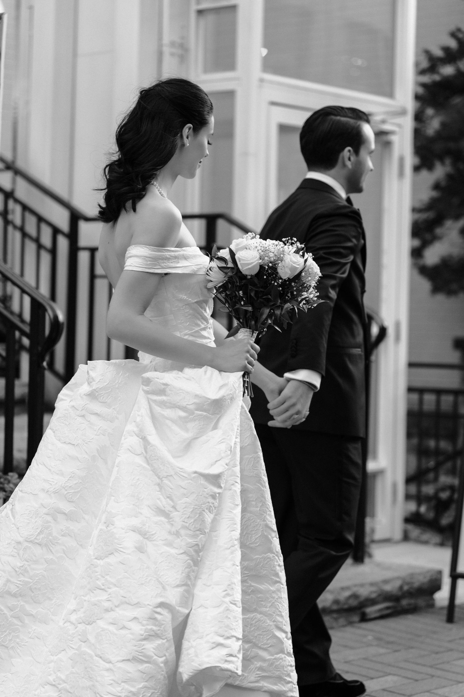 Three bridesmaids in white dresses walk together during a formal wedding event with black and white photography.