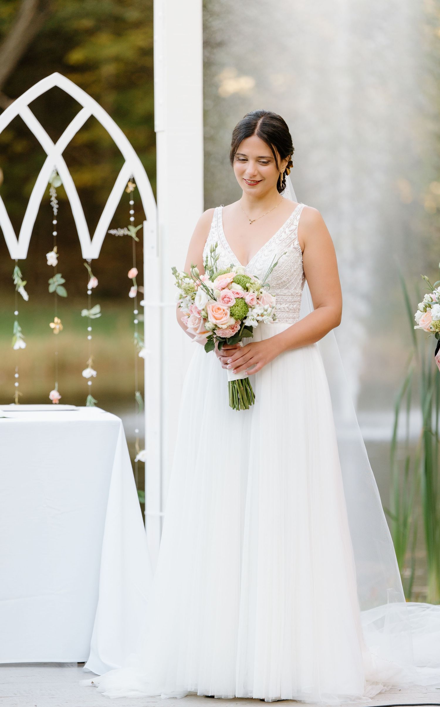 Elegant outdoor wedding ceremony with decorative white arch and floral bouquet.