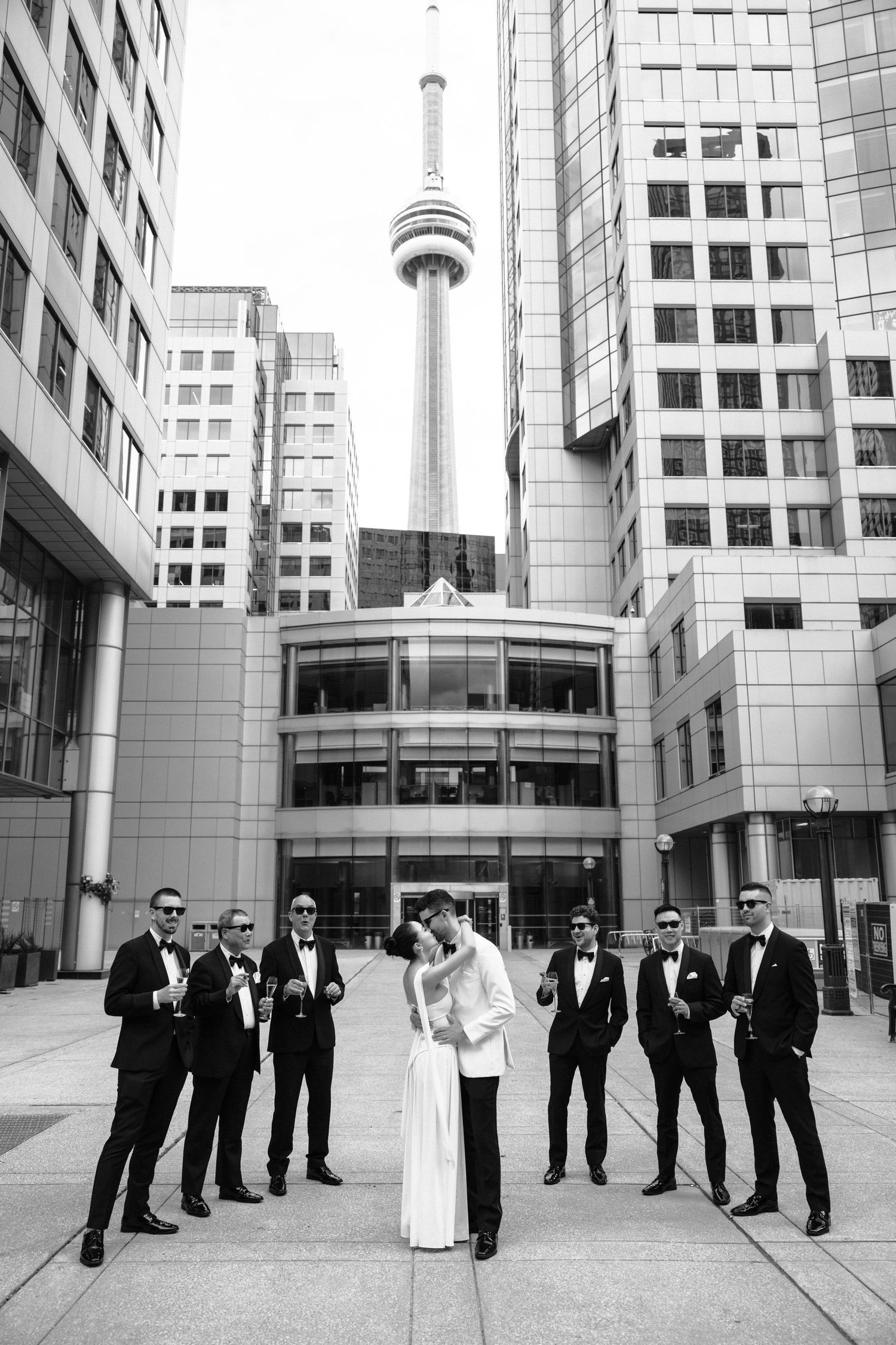 Black and white wedding photo with CN Tower and modern buildings in downtown Toronto's urban cityscape backdrop.