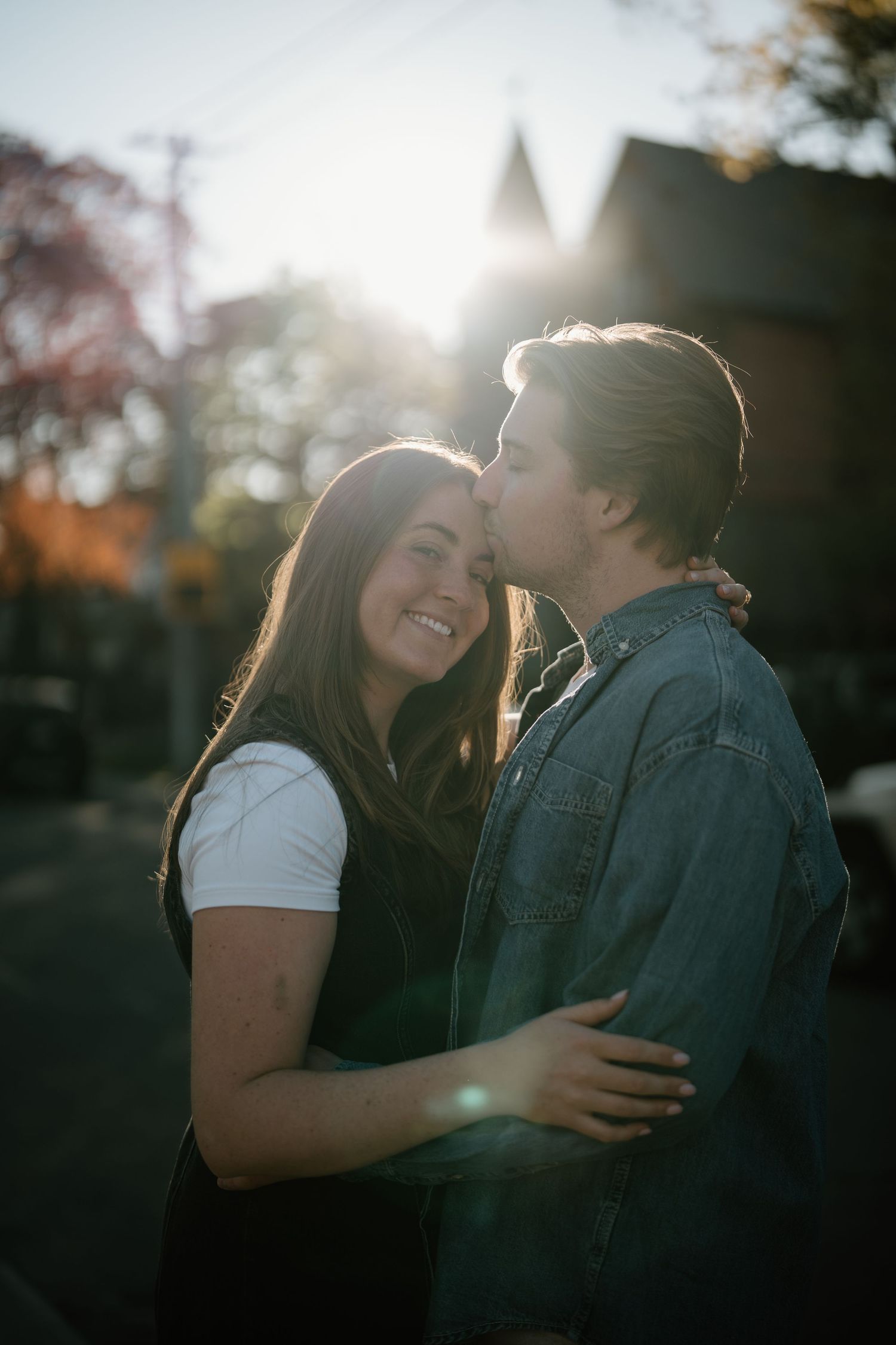A romantic couple shares a tender moment in the golden evening sunlight against a blurred outdoor background.