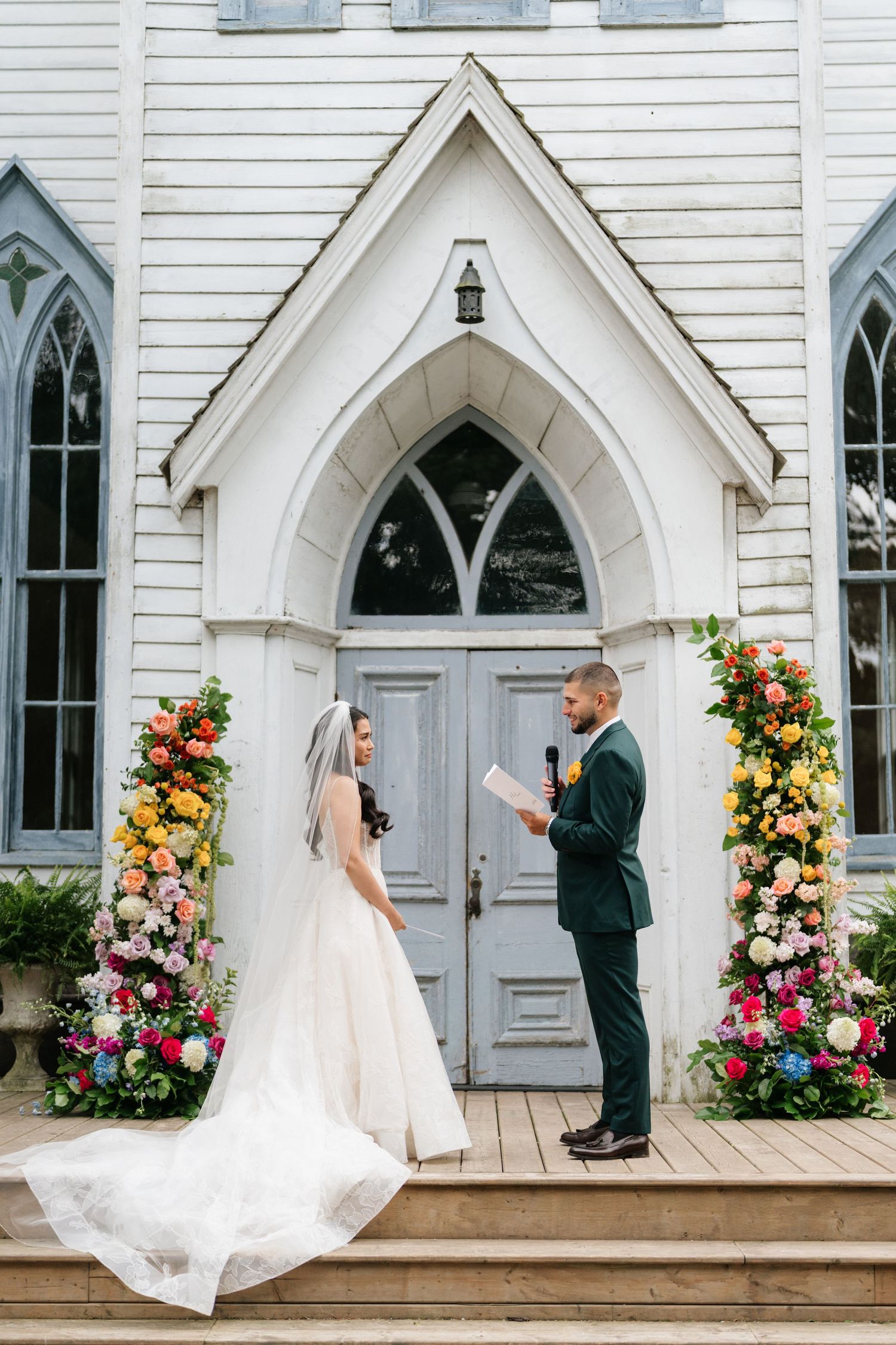 Wedding ceremony at a charming white chapel with Gothic windows and colorful floral arrangements.