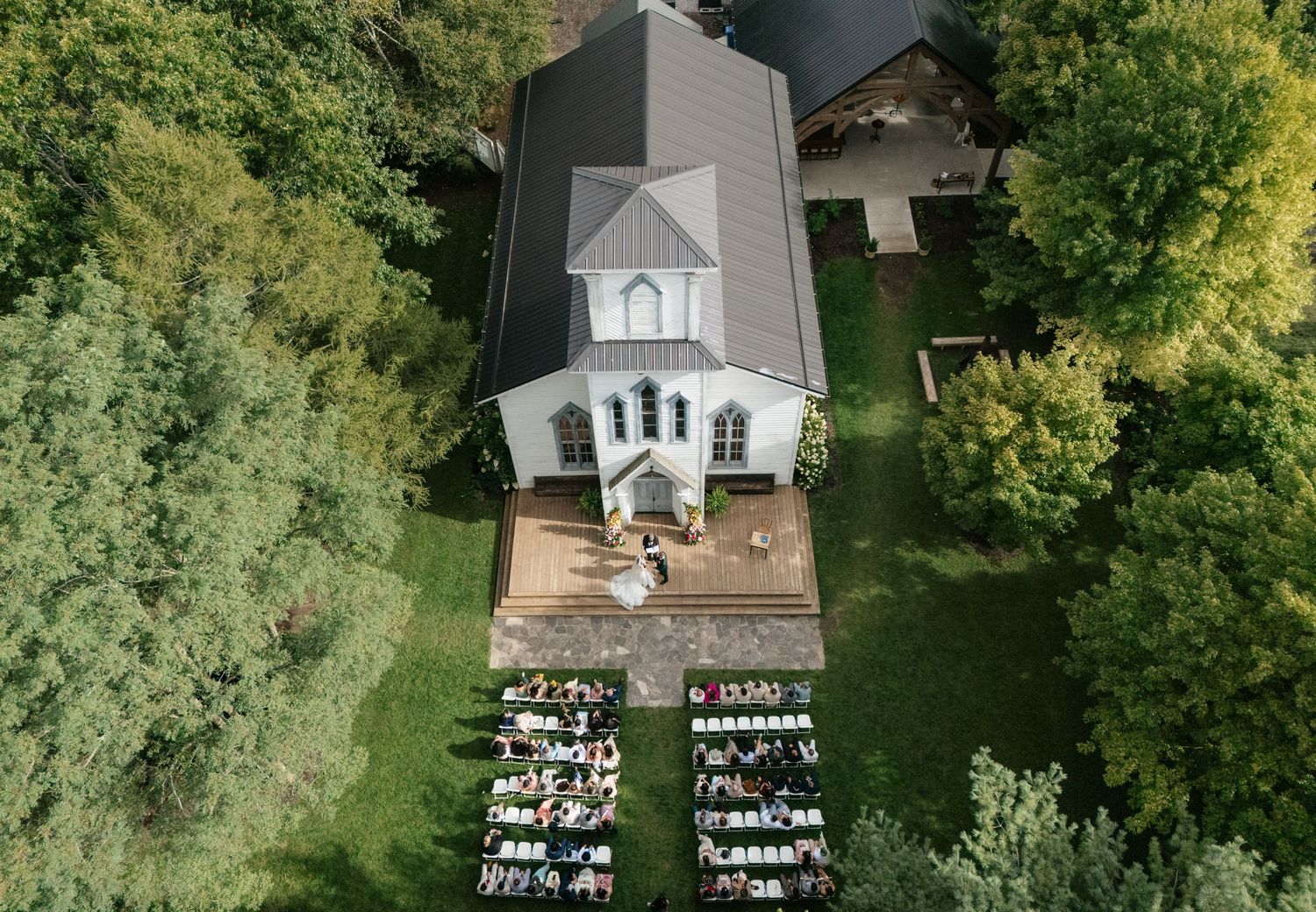 Bird's eye view of a white church with outdoor seating arranged symmetrically for a wedding ceremony.