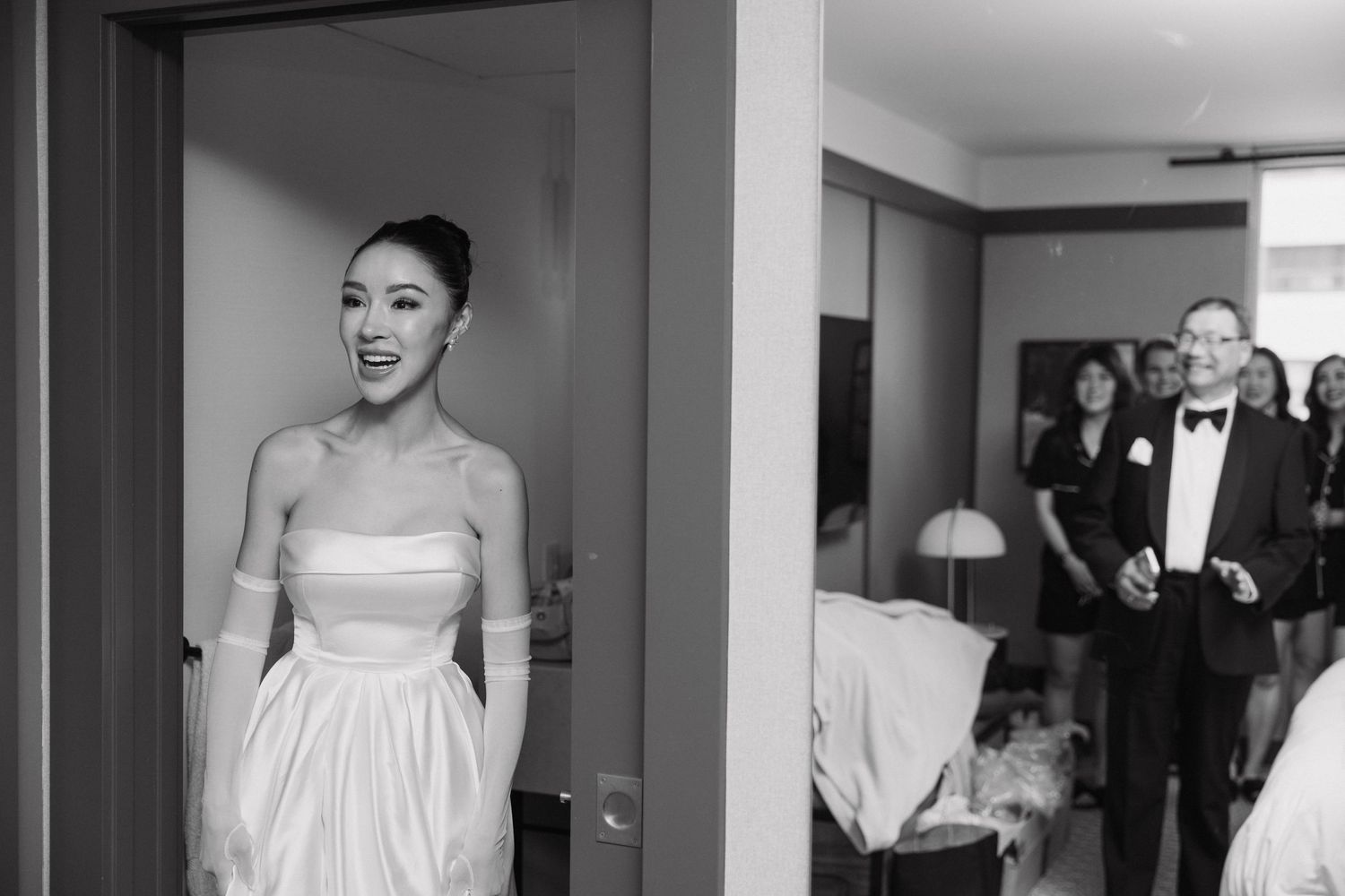 A black and white photo of someone in a strapless wedding dress emerging from a doorway.