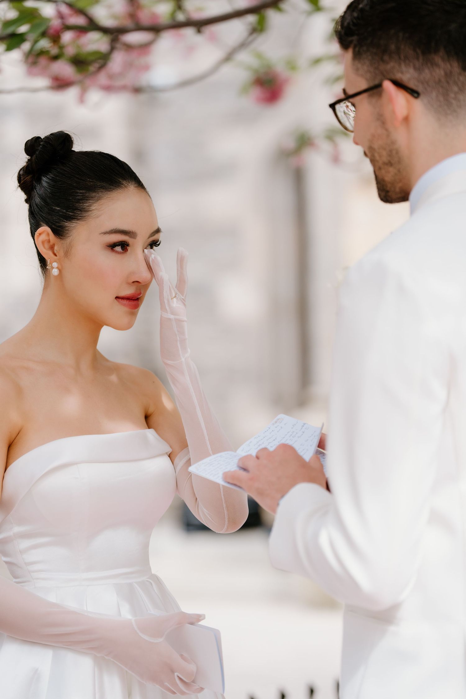 A bride and groom exchange vows during an elegant wedding ceremony with cherry blossoms in the background.