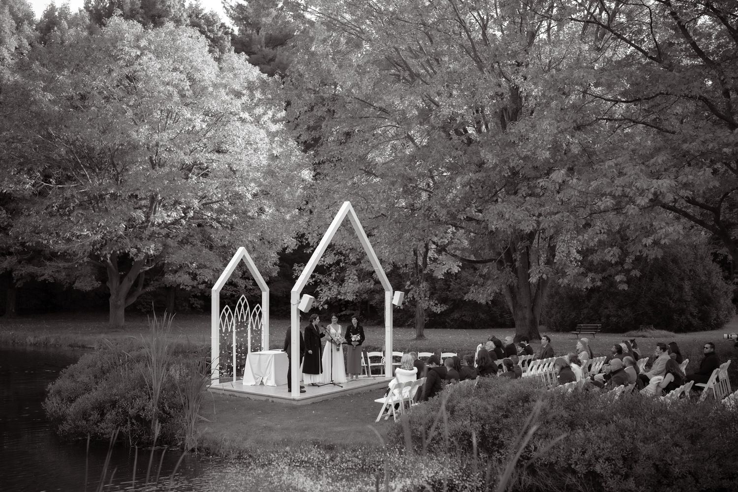 Wedding ceremony setup with white gothic arches against golden autumn trees.