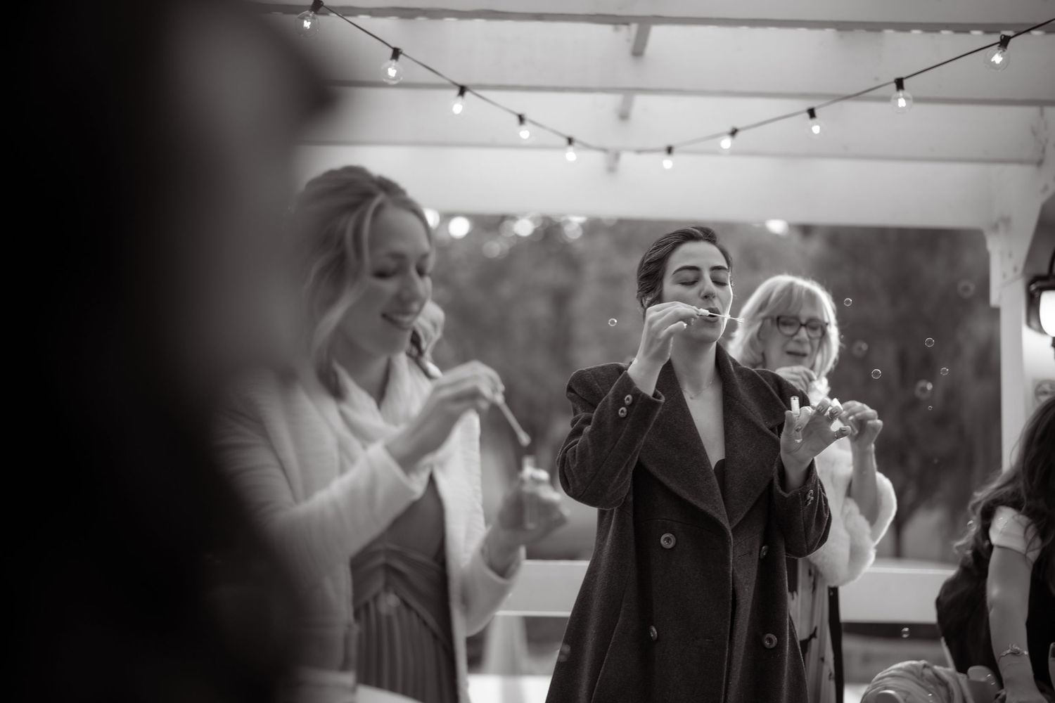 Black and white photo of wedding guests enjoying a celebration under string lights.