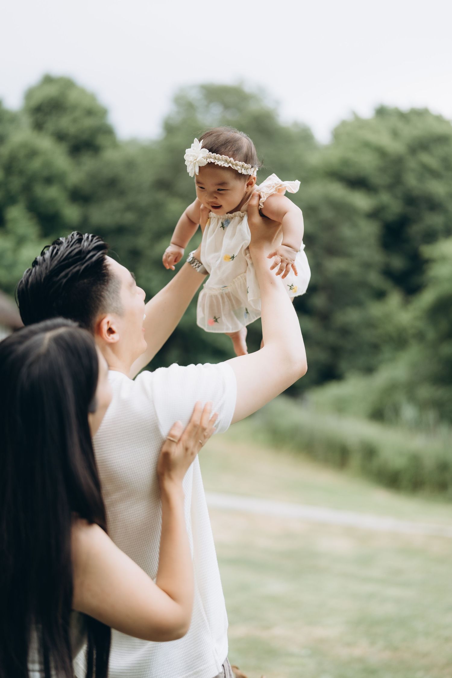 A sweet moment captured outdoors as parents lift their baby wearing a floral headband.
