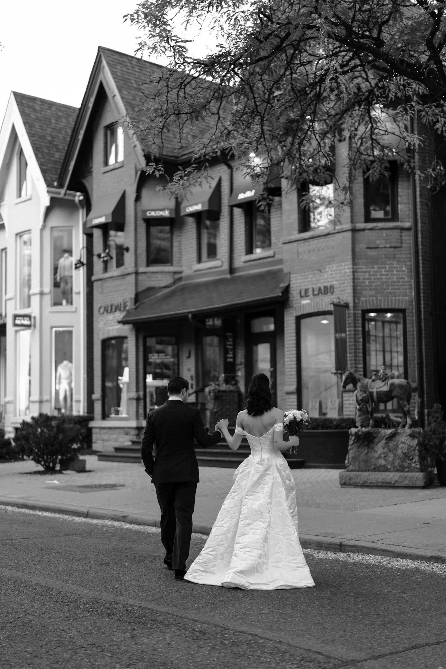 A black and white wedding photo sequence shows a couple walking down a charming small town street lined with shops.