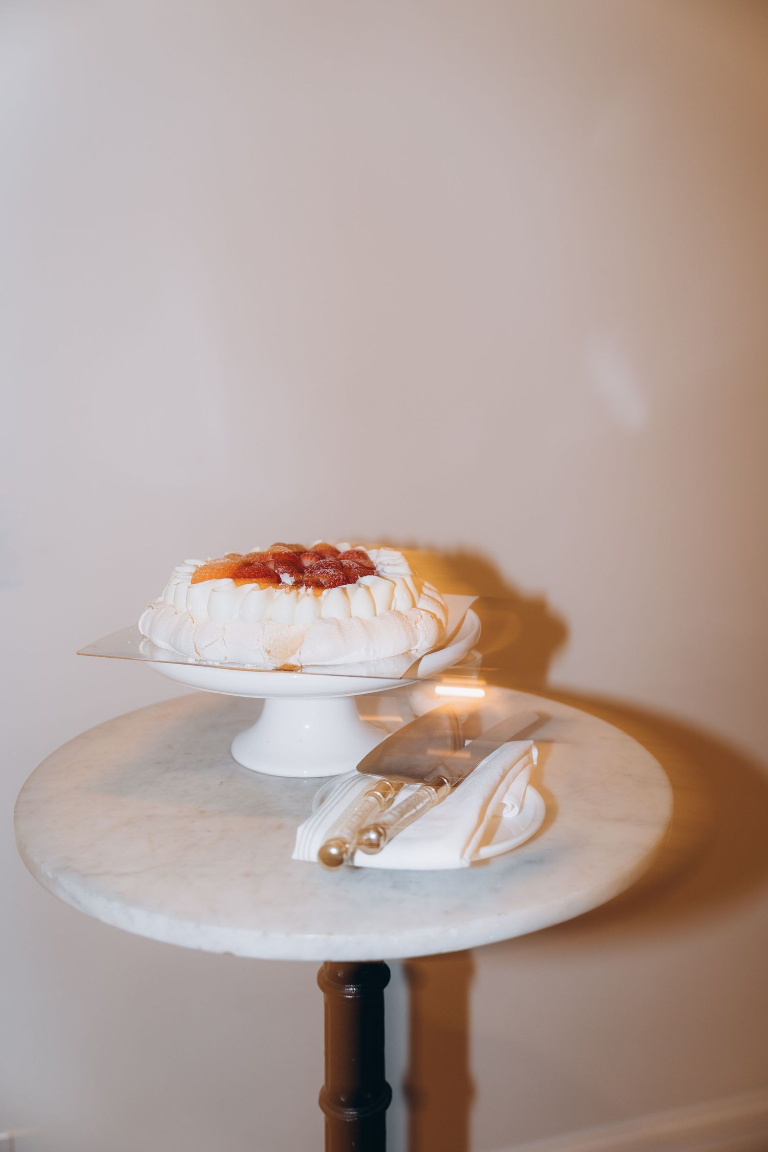 A simple white decorative hat displayed on a white pedestal against a neutral beige background.