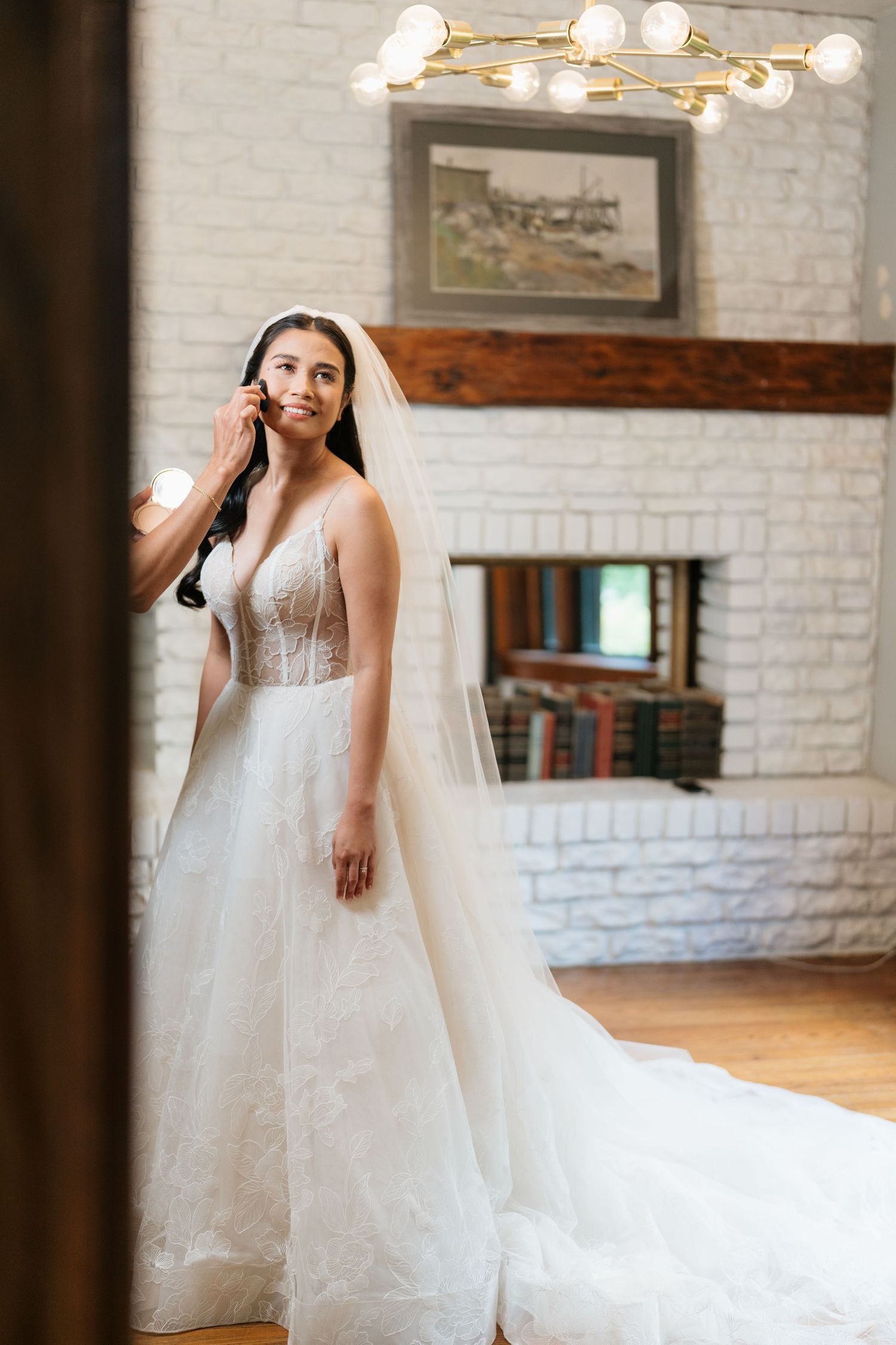 A bride in a flowing white tulle wedding gown poses in an elegant room with white brick walls and warm lighting.