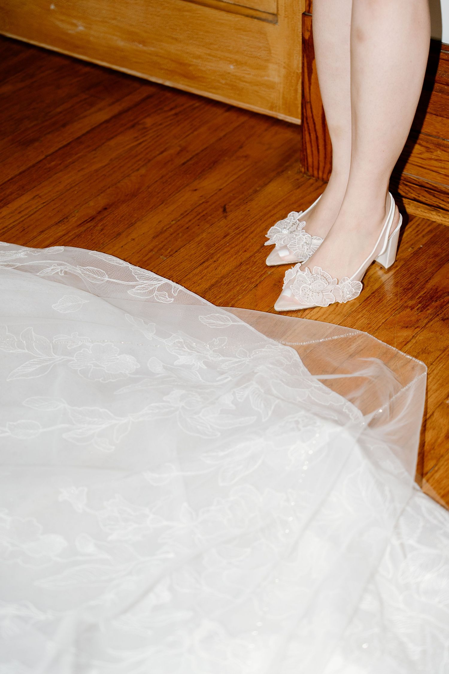 Close-up view of white ballet shoes and tulle fabric on a hardwood floor.