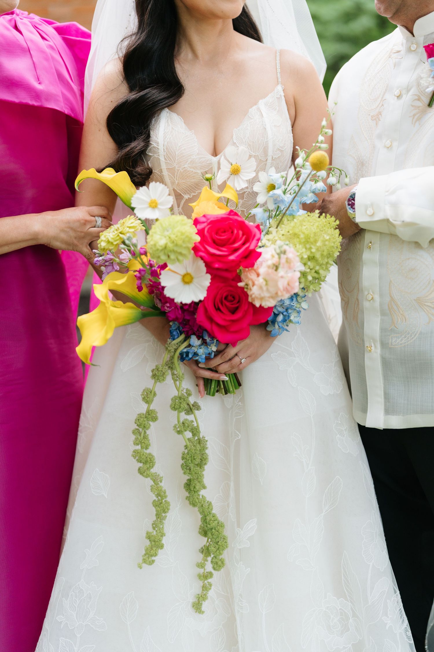 Vibrant wedding bouquet featuring red roses, yellow lilies, white daisies and cascading greenery against a white dress.